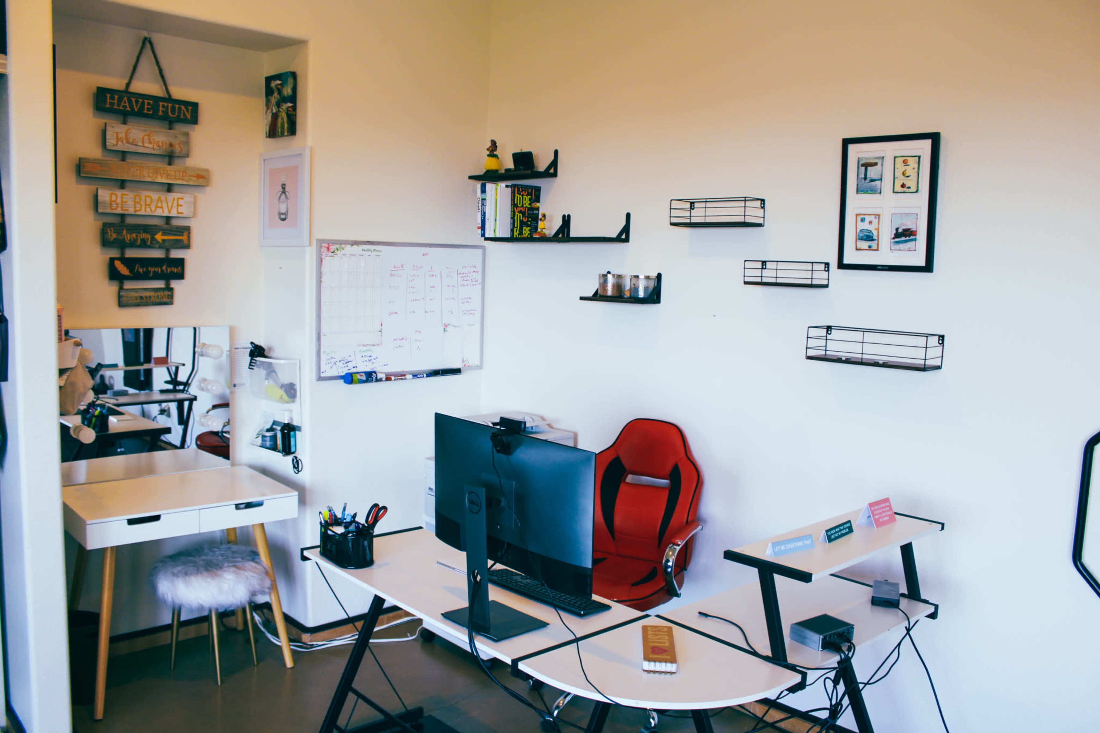 A modern workspace featuring a desk with a computer, a red ergonomic chair, wall shelves, and a whiteboard with a calendar.