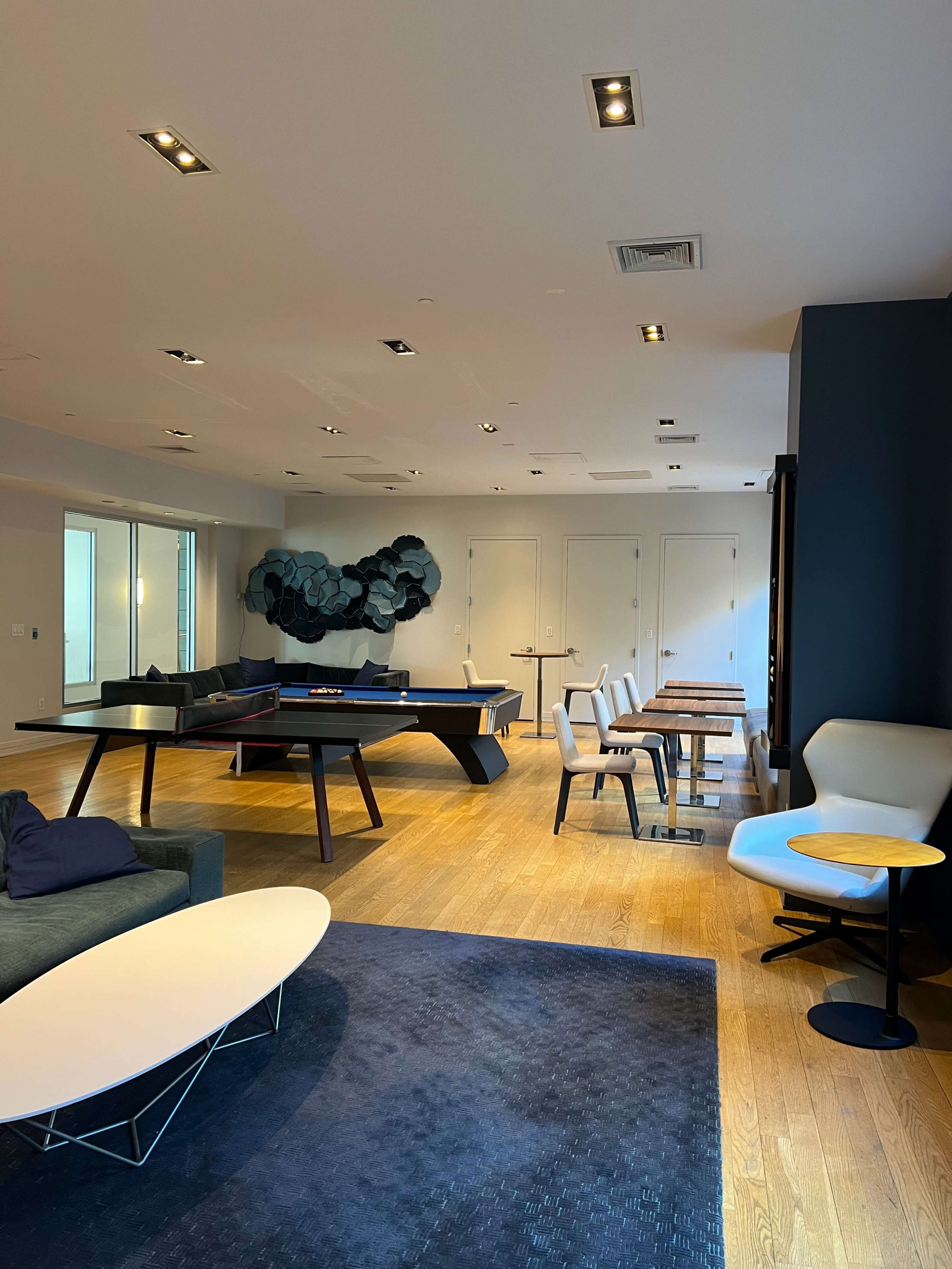 A modern lounge area with a billiard table, several seating options, and a wall adorned with abstract art.