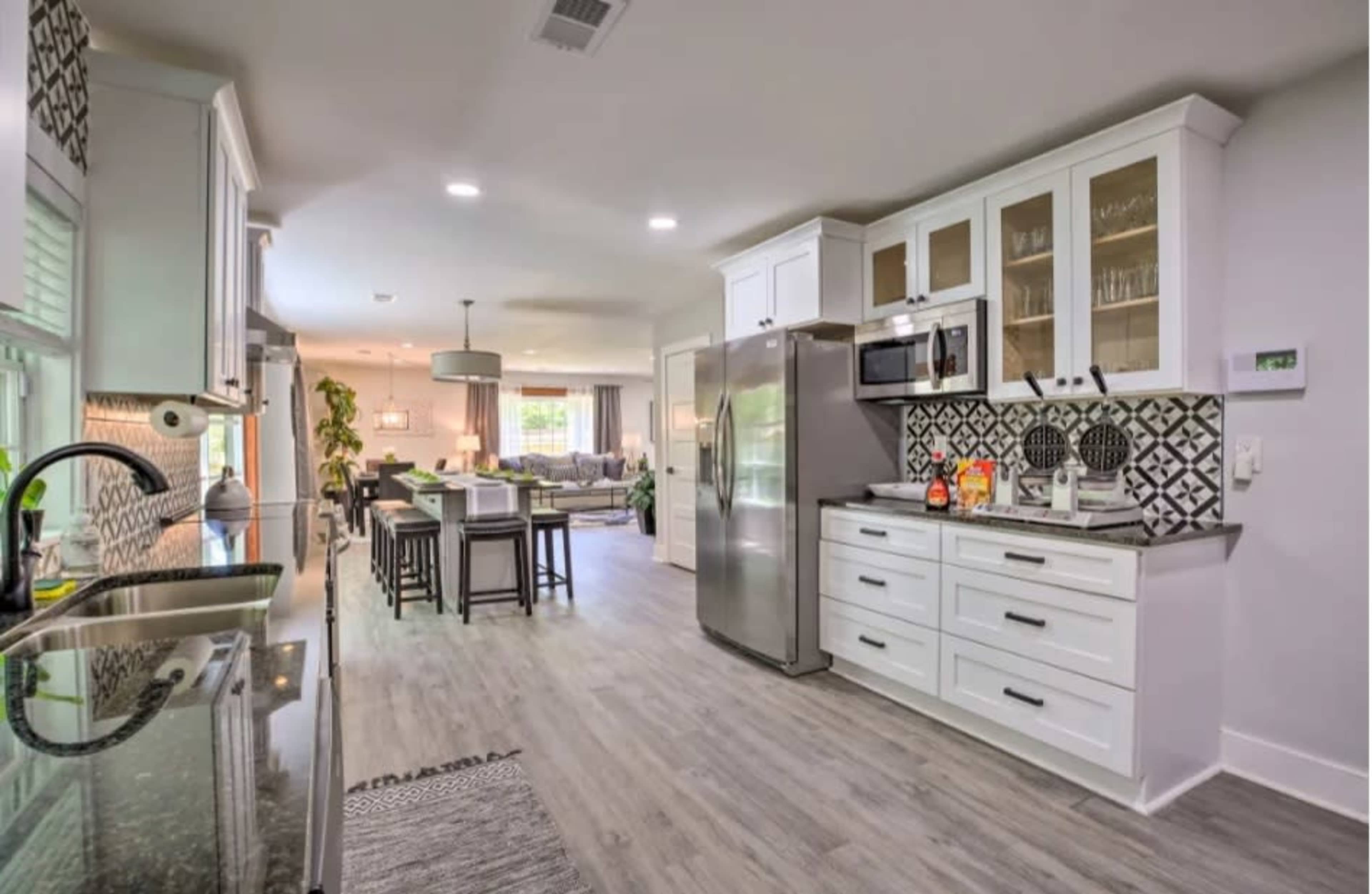 A modern kitchen with white cabinetry, a stainless steel refrigerator, and a view into a dining area and living room beyond.
