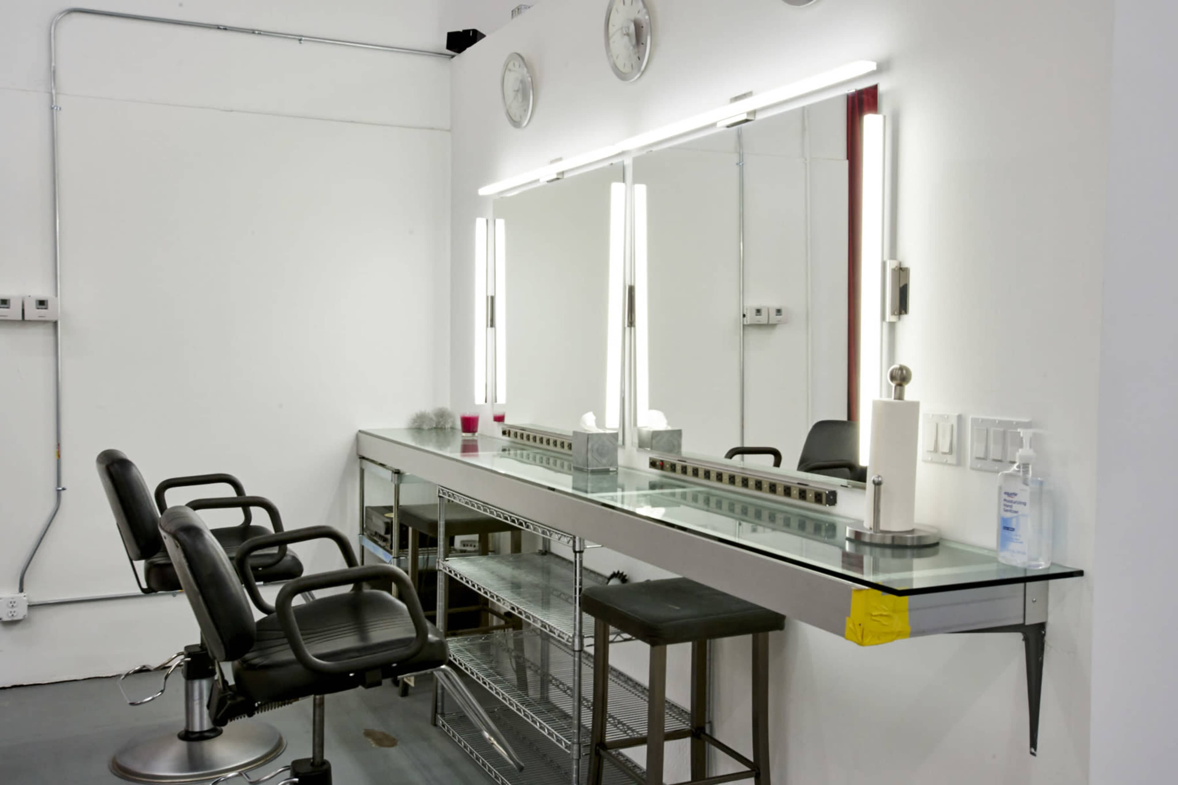 A minimalist hair salon with two styling chairs and a long mirror under bright lighting.