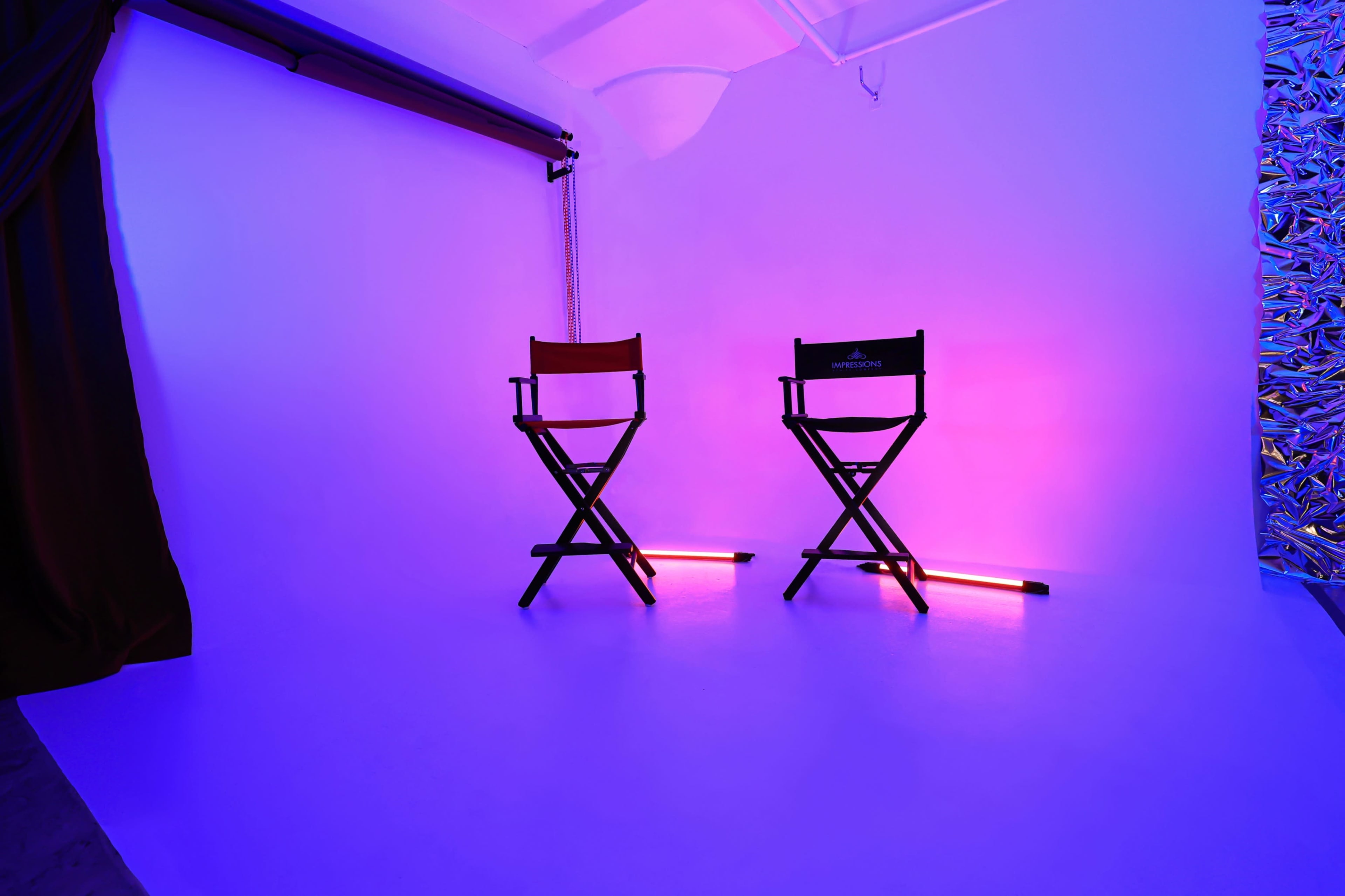 A photography studio with two director's chairs set against a brightly lit purple backdrop.