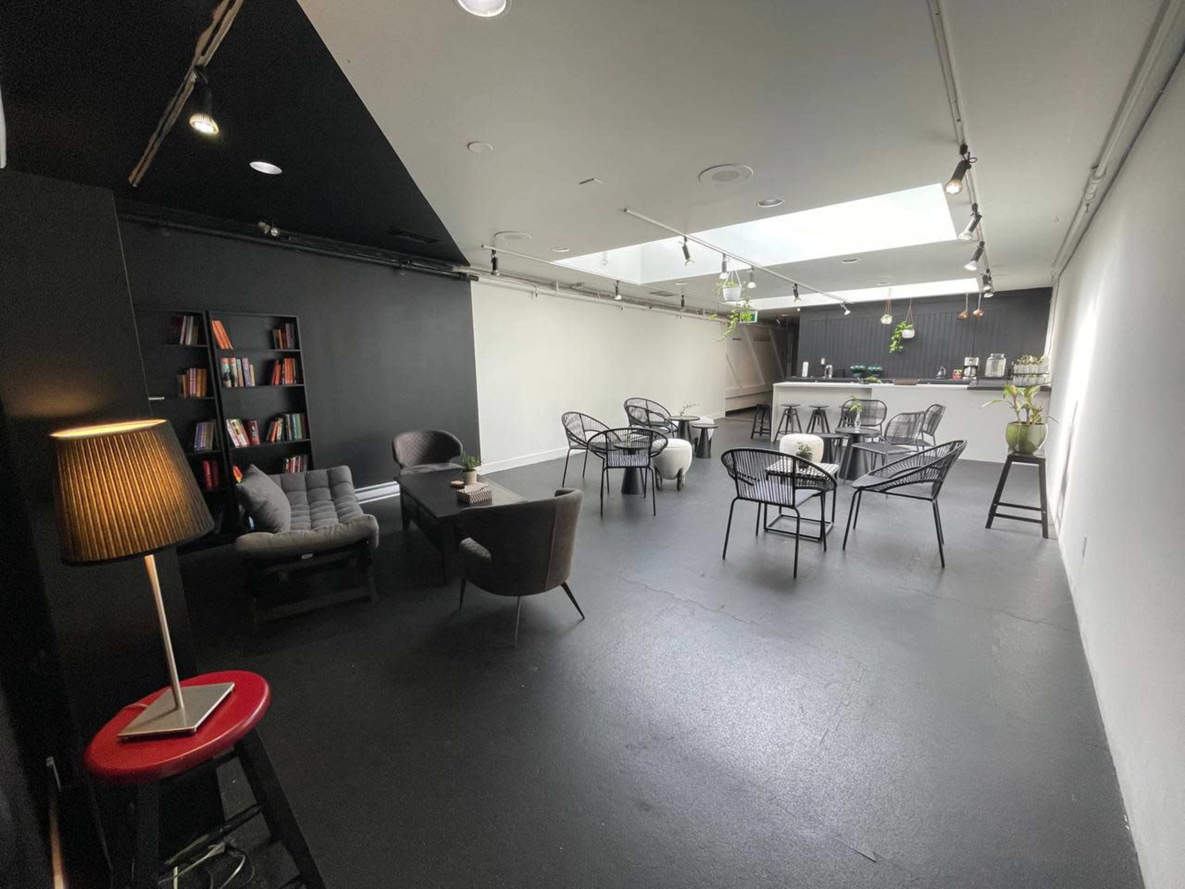 A spacious, modern interior with black flooring, a bar area, several tables and chairs, and a bookshelf against one wall.
