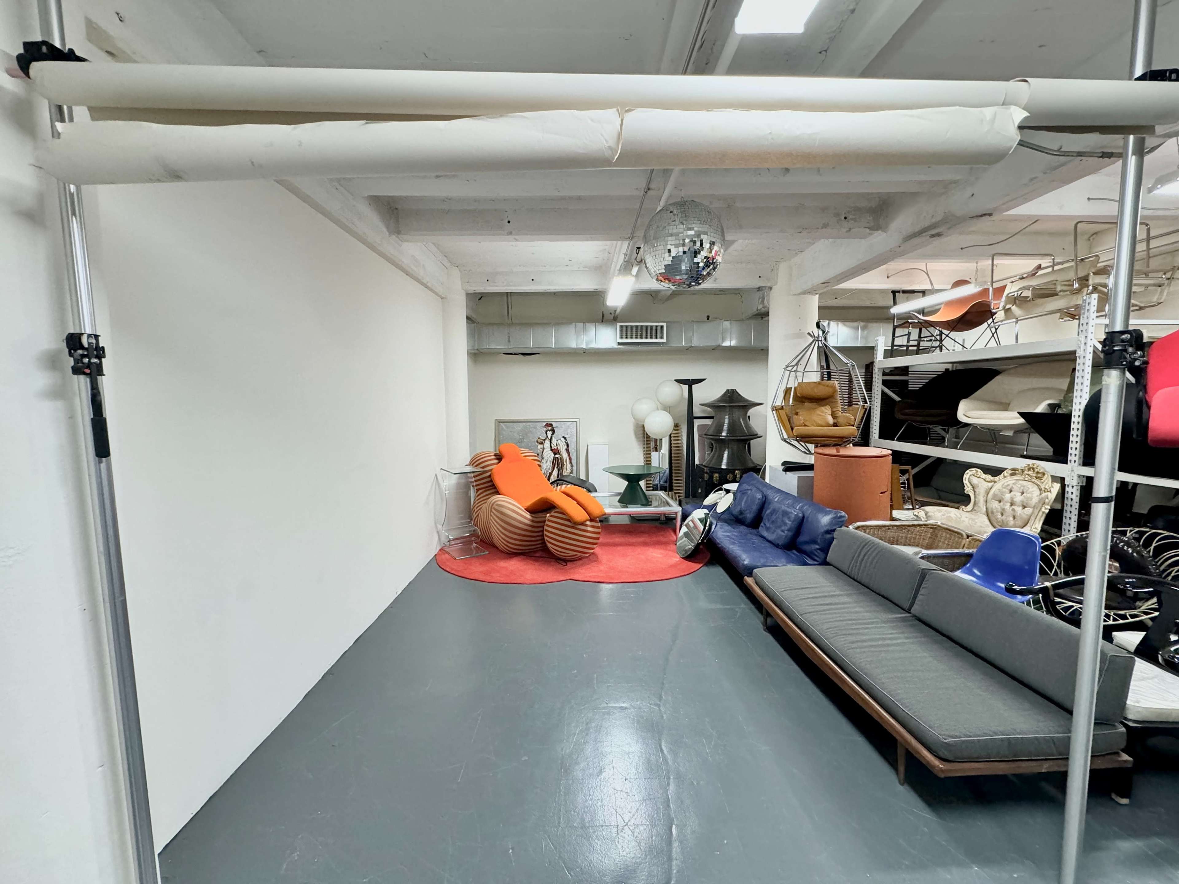 A spacious interior with a gray floor, featuring a variety of furniture, including a large gray sofa, an orange chair, and a round red rug, against a plain white wall.
