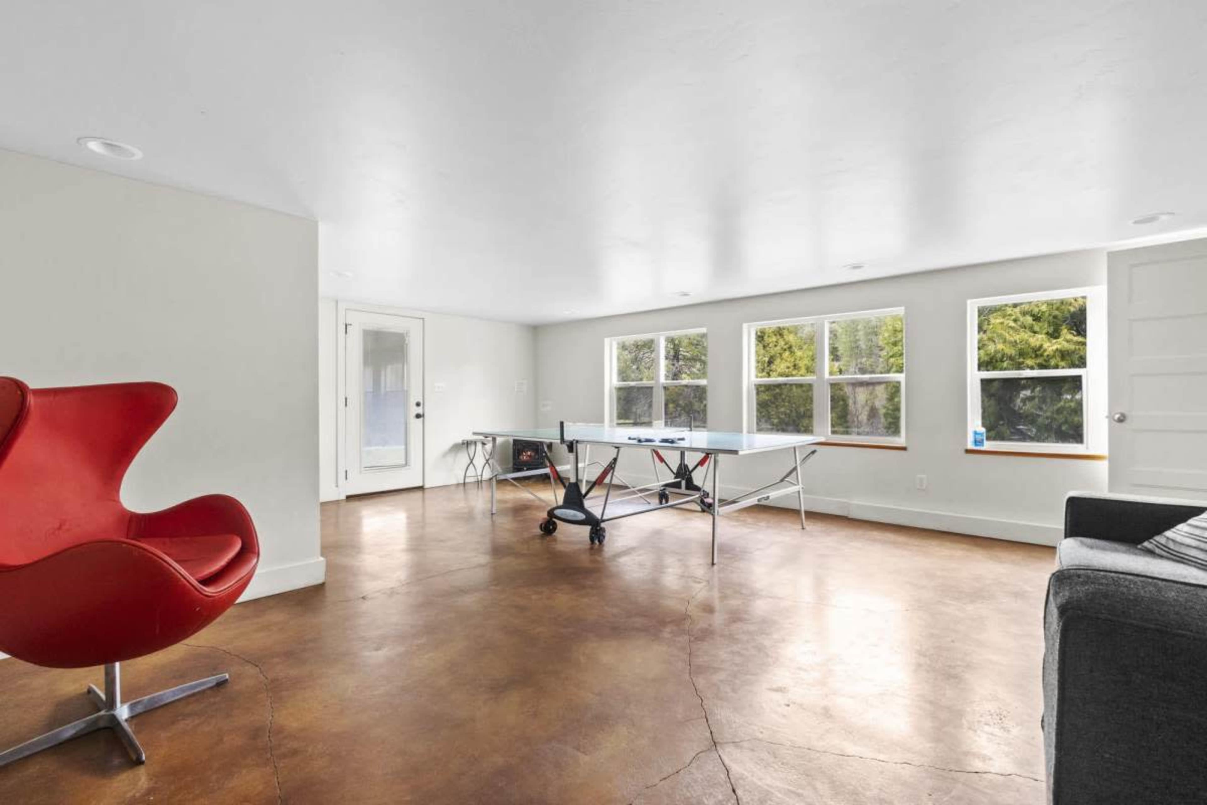 A spacious room with a table, red chair, and large windows allowing natural light.