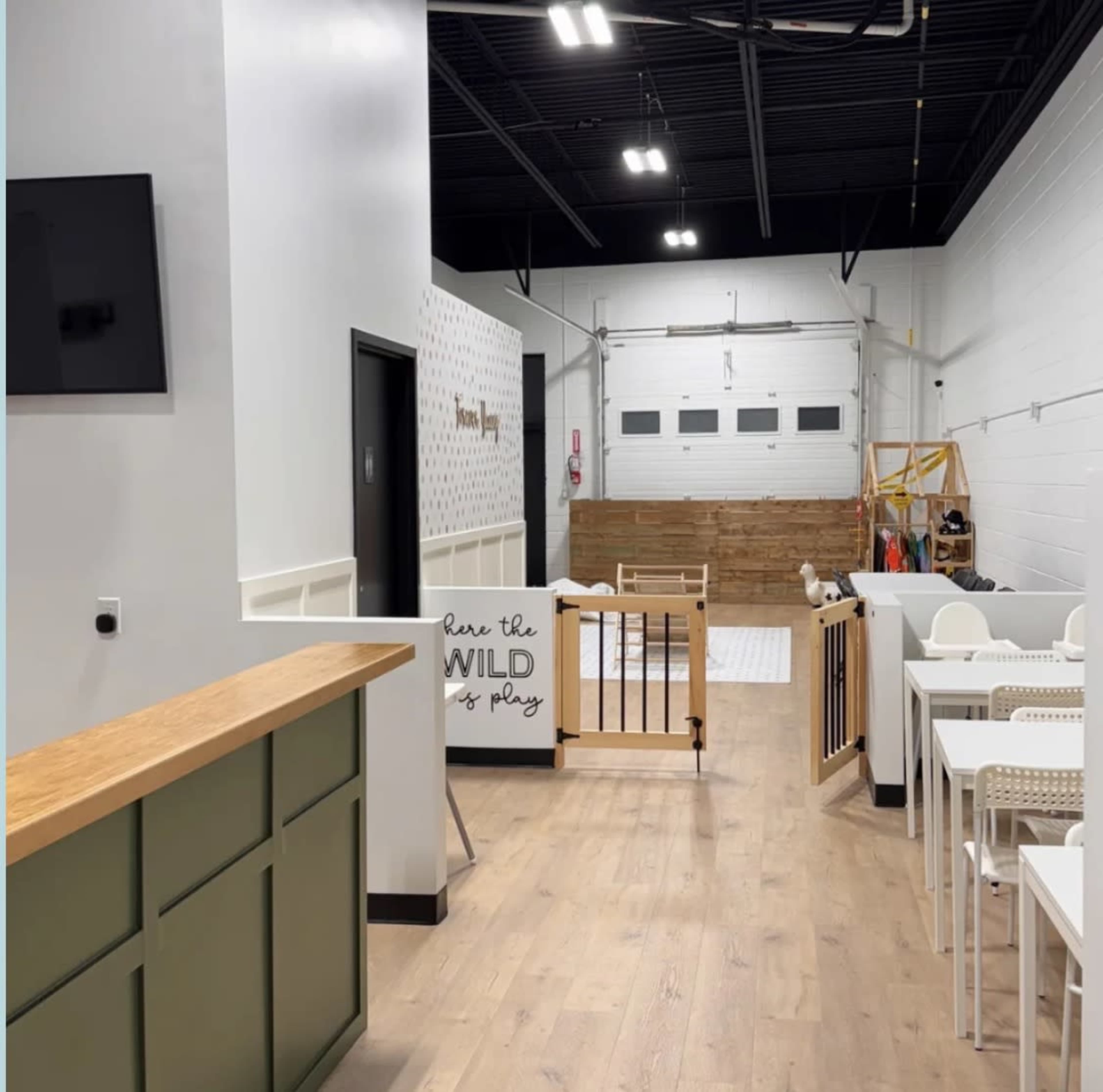 The image shows the interior of a spacious play area for children, featuring wooden flooring, a reception desk, and various play equipment in the background.