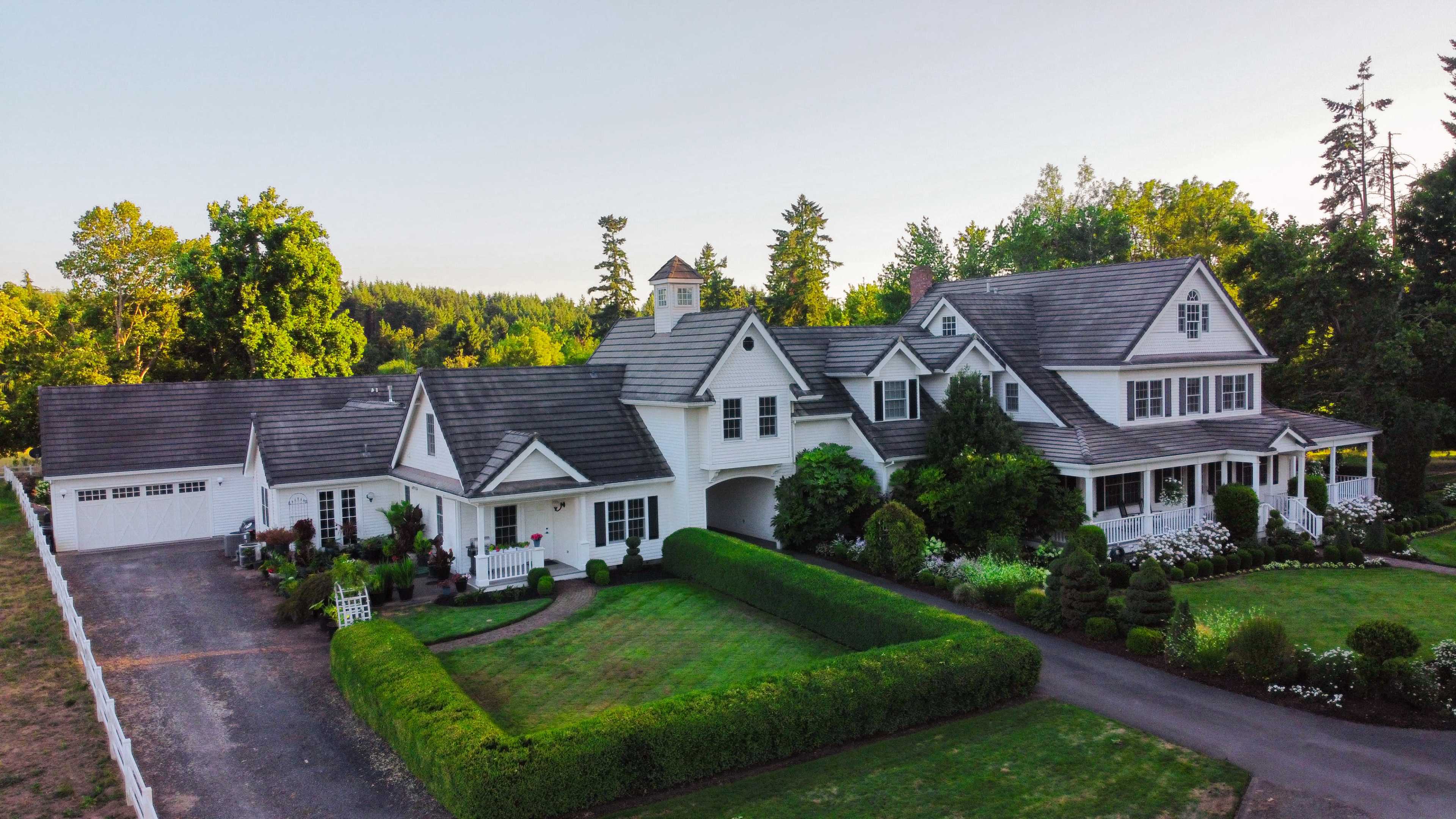 A large, white colonial-style house with a well-manicured lawn and surrounding trees.