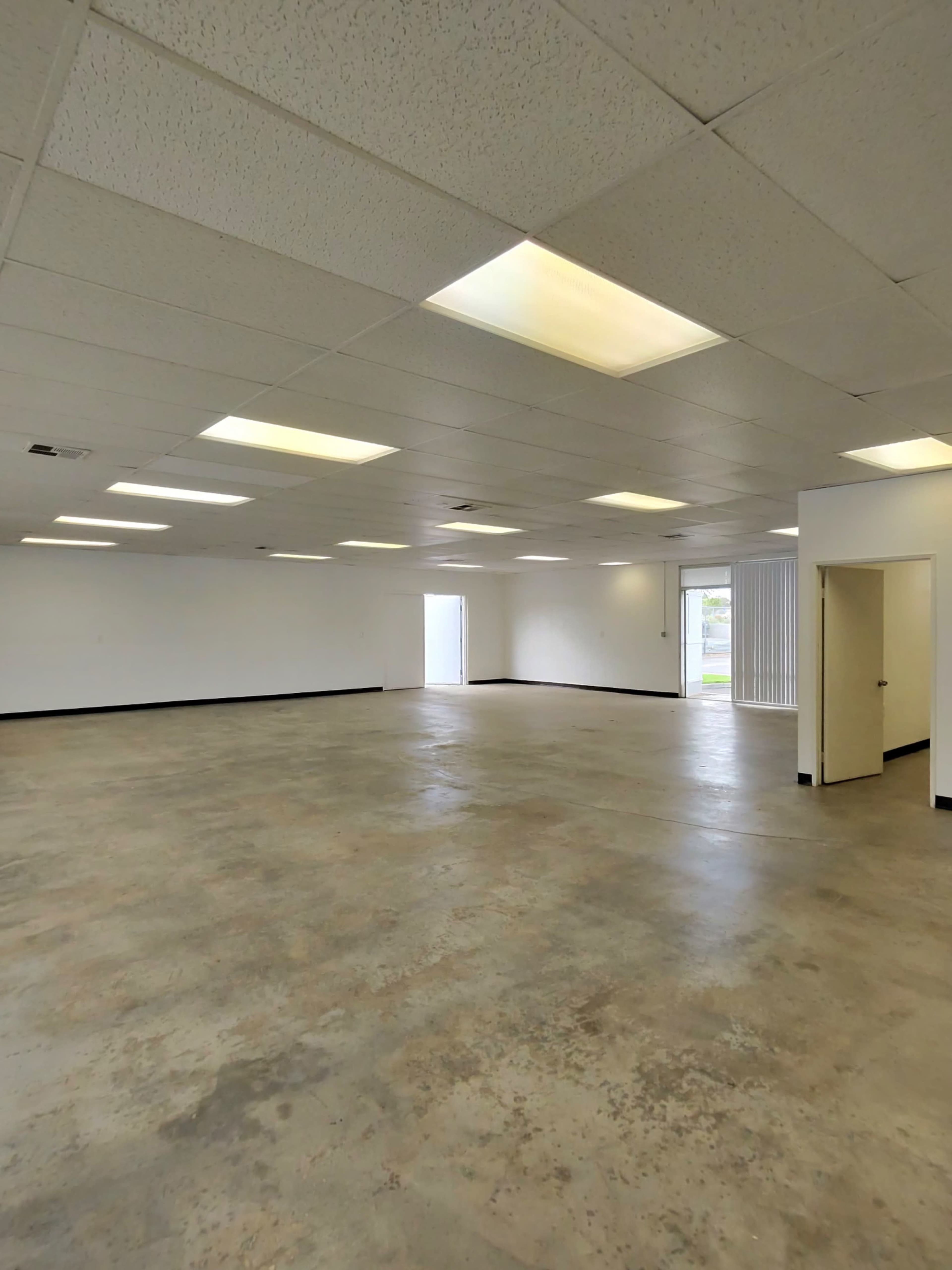 The image shows a spacious, empty commercial room with concrete flooring and fluorescent lights.
