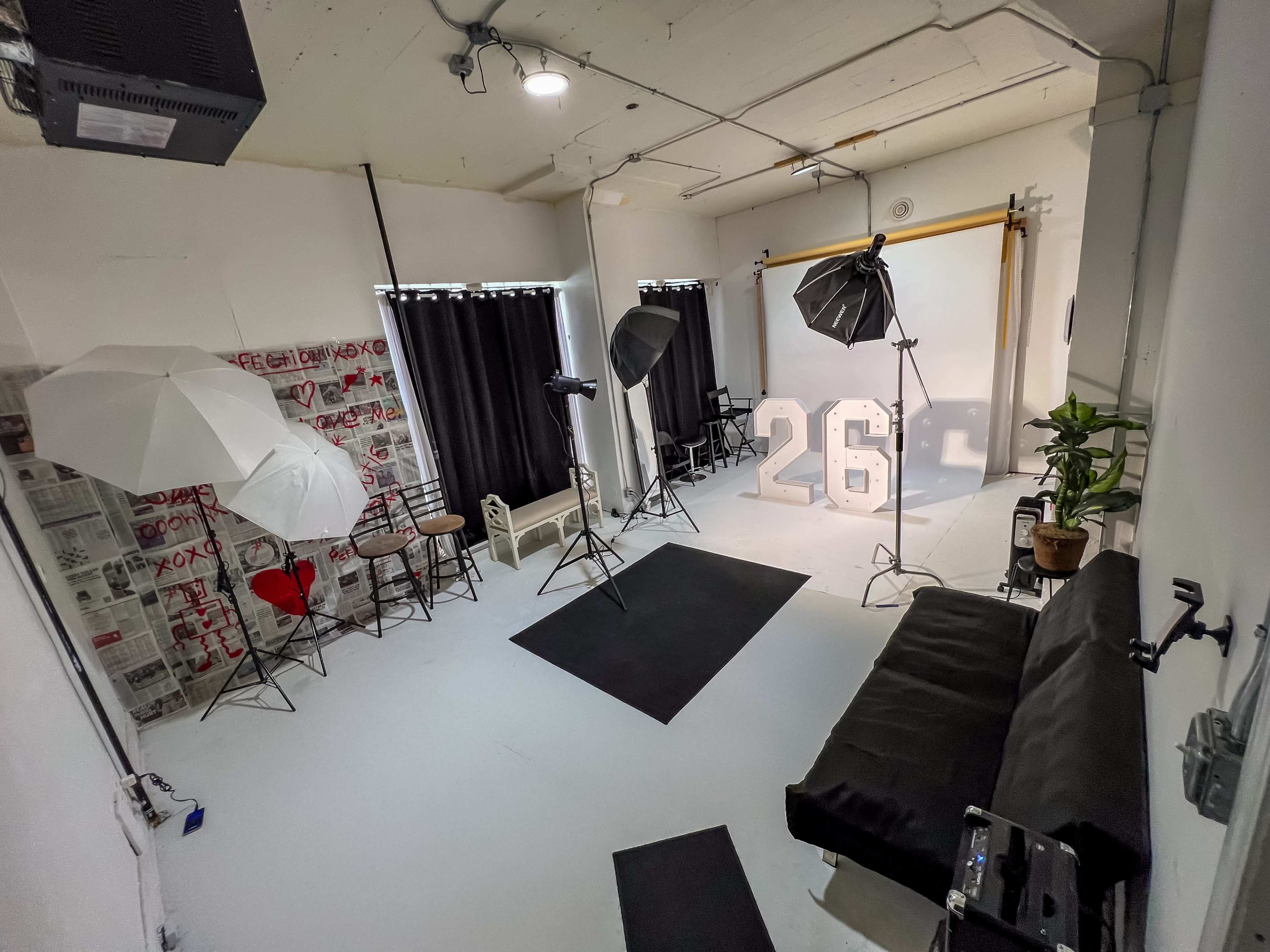 The image shows a photography studio equipped with lighting equipment, a backdrop, and large illuminated numbers "26" in the center.
