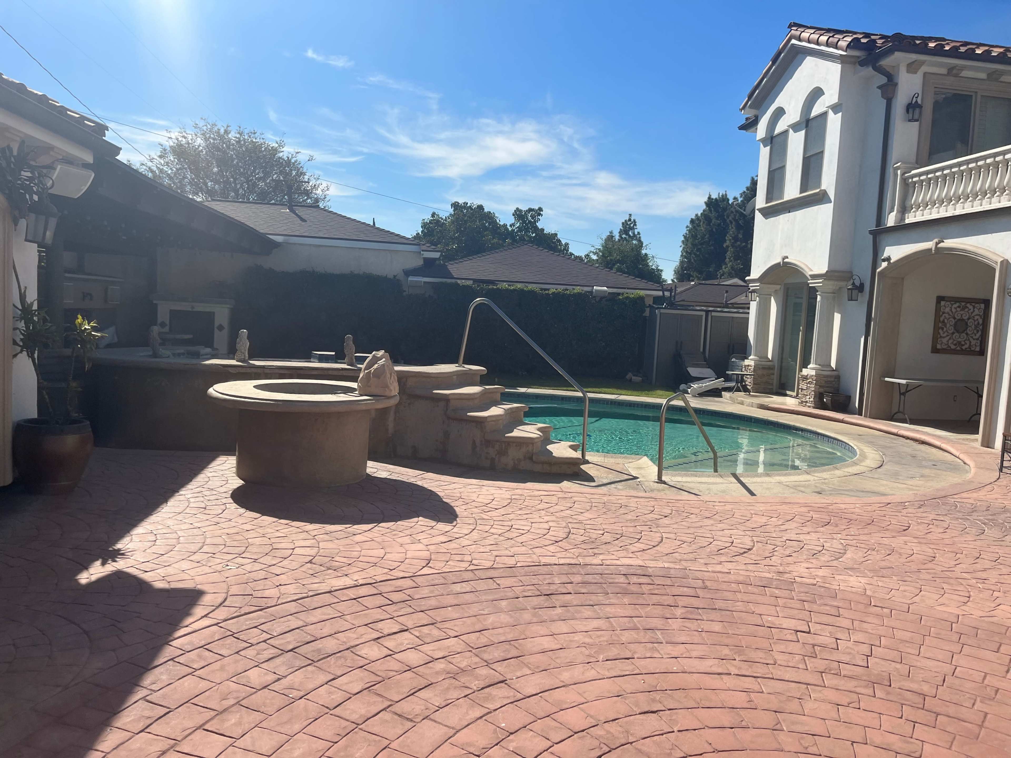 A backyard with a swimming pool and a raised hot tub, surrounded by a patio with stamped concrete and adjacent to a house.