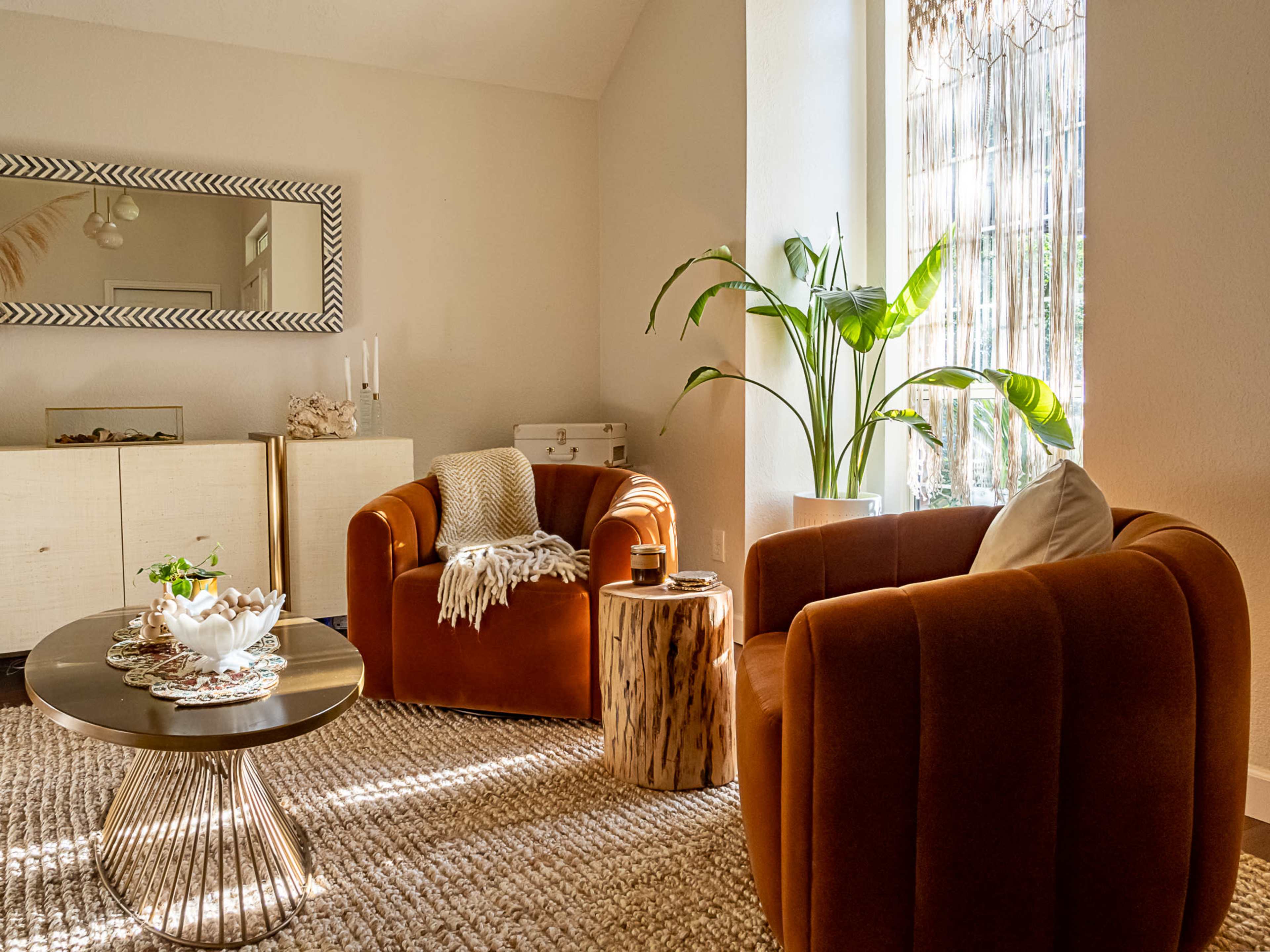 A cozy living room features two orange armchairs, a round coffee table, and a large window with a potted plant.