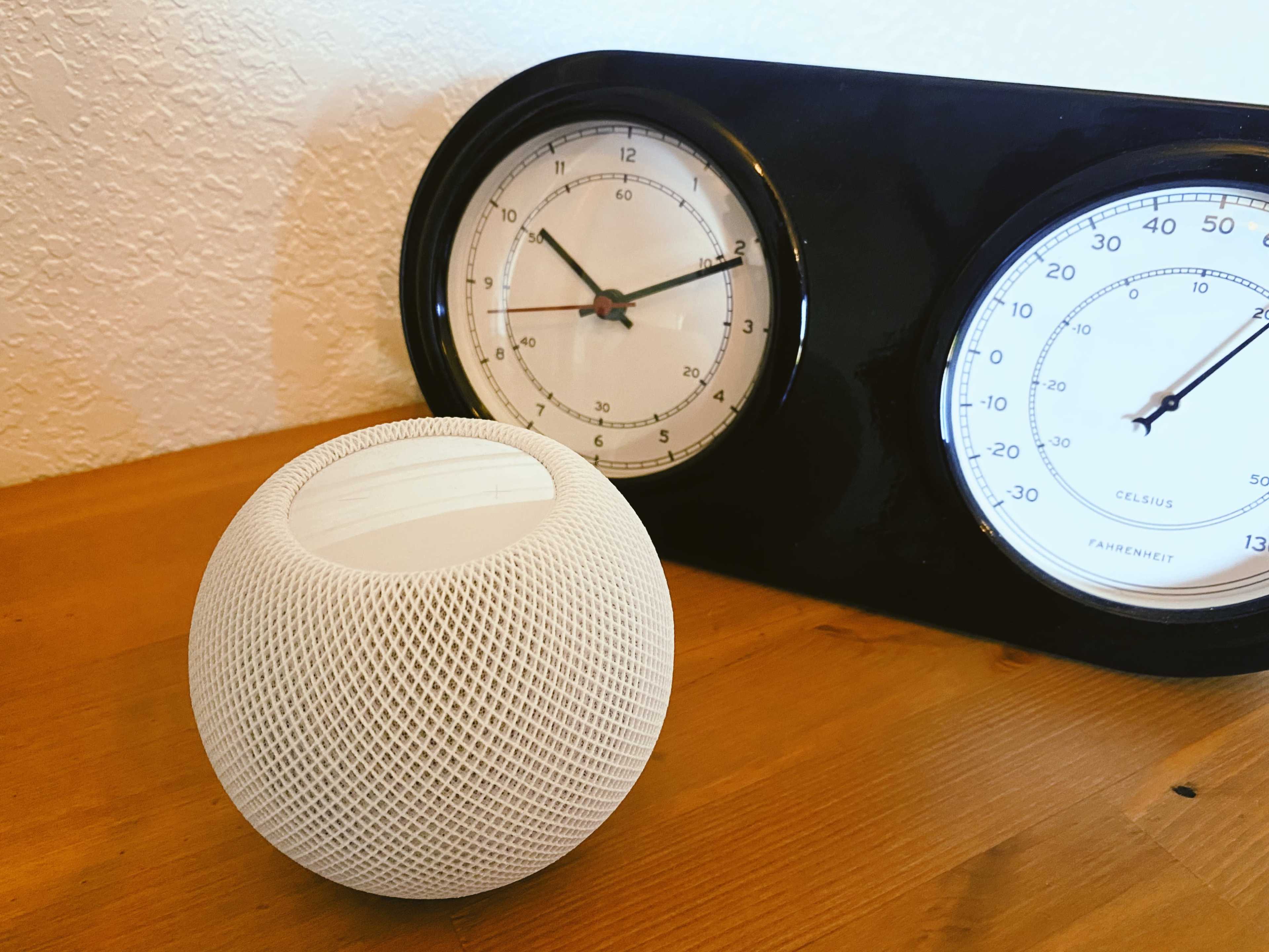 A textured white spherical object is placed on a wooden table next to a black clock featuring two dials for time and temperature.