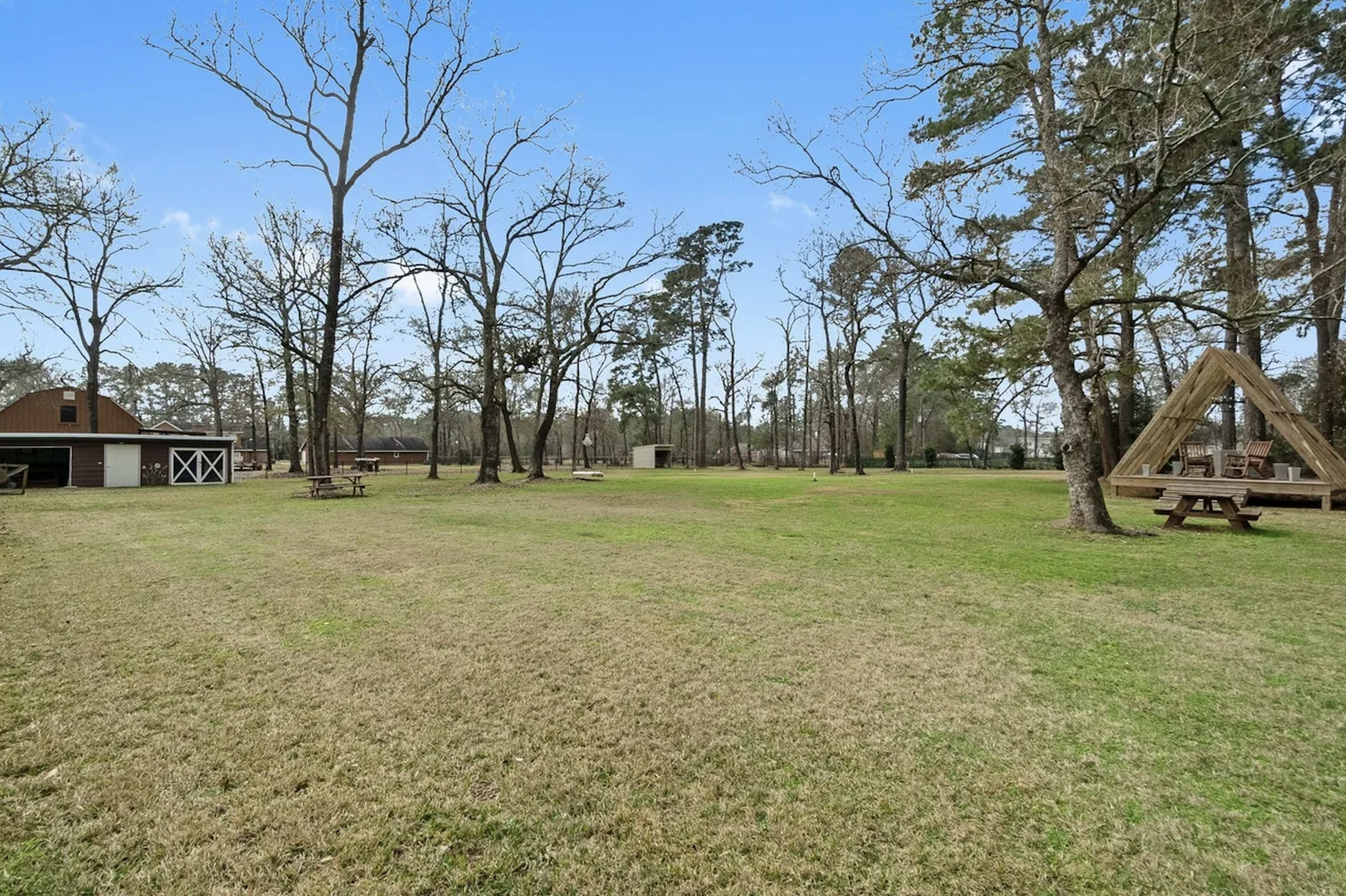 The image shows an open grassy area surrounded by bare trees, with a barn and picnic table in the background.