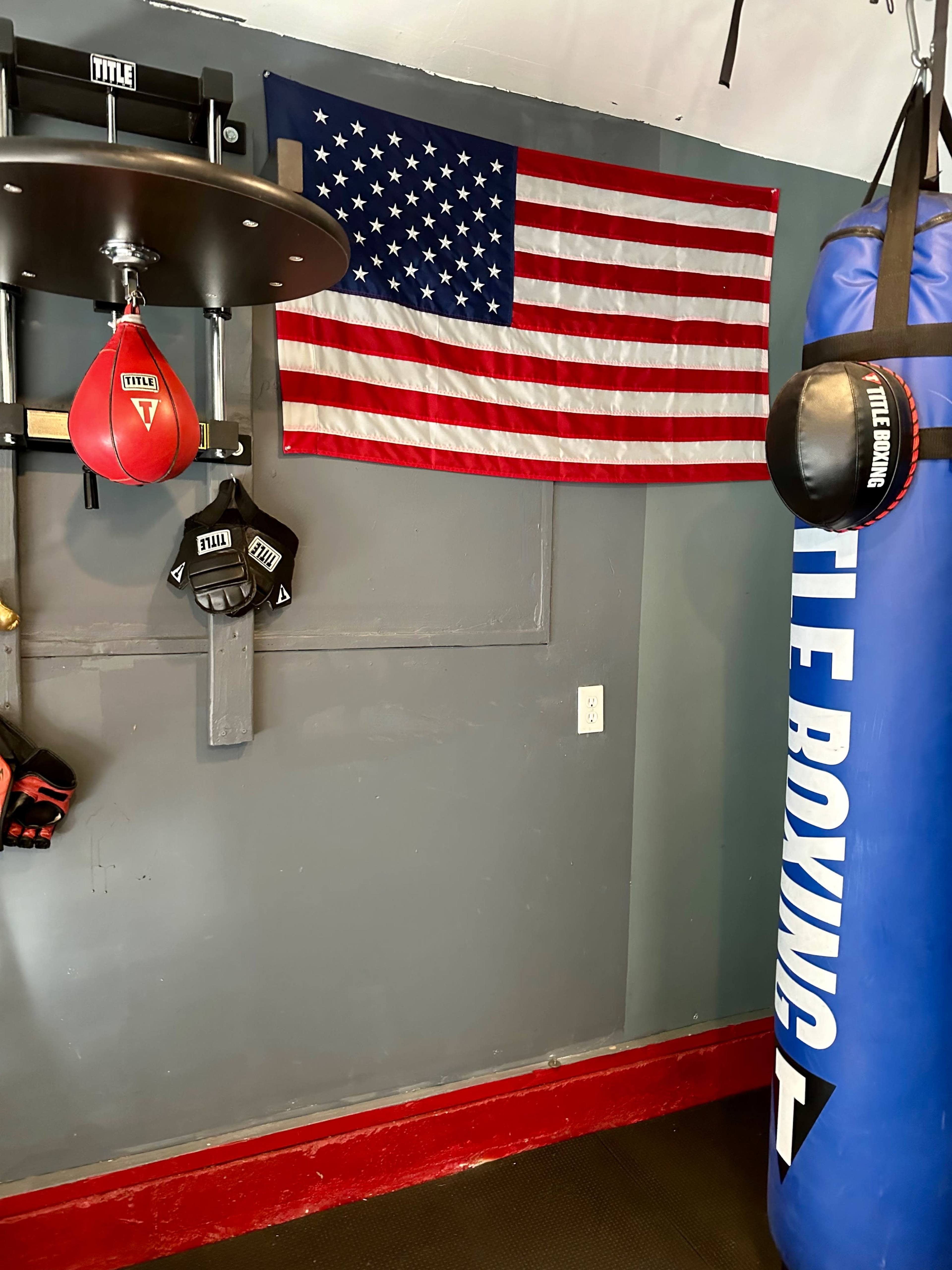 A boxing training area featuring a blue punching bag, boxing gloves, and an American flag mounted on the wall.