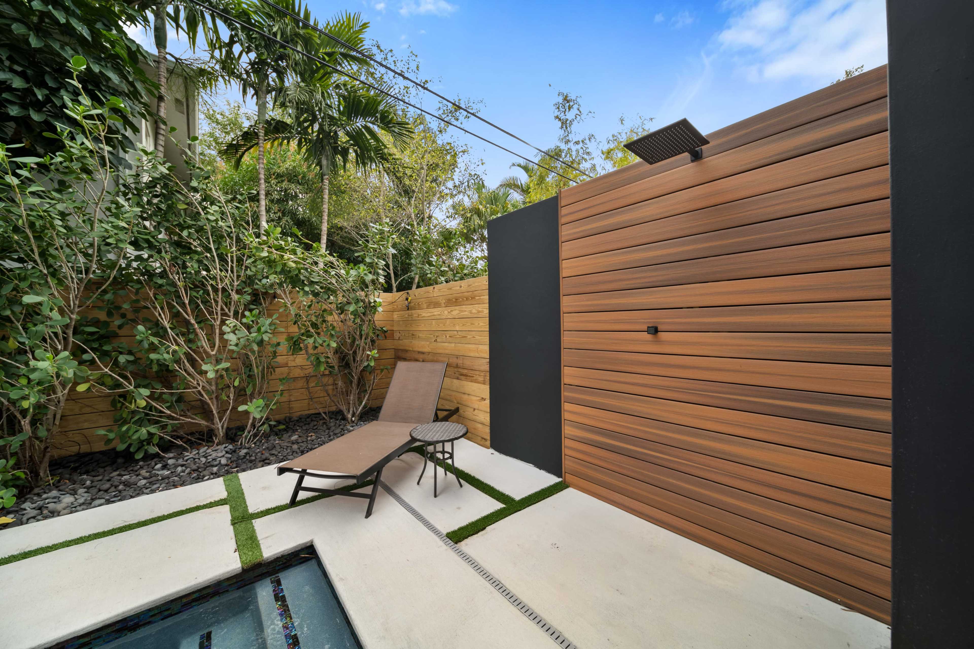 A lounge chair rests beside a small, landscaped pool surrounded by wooden fences and greenery.