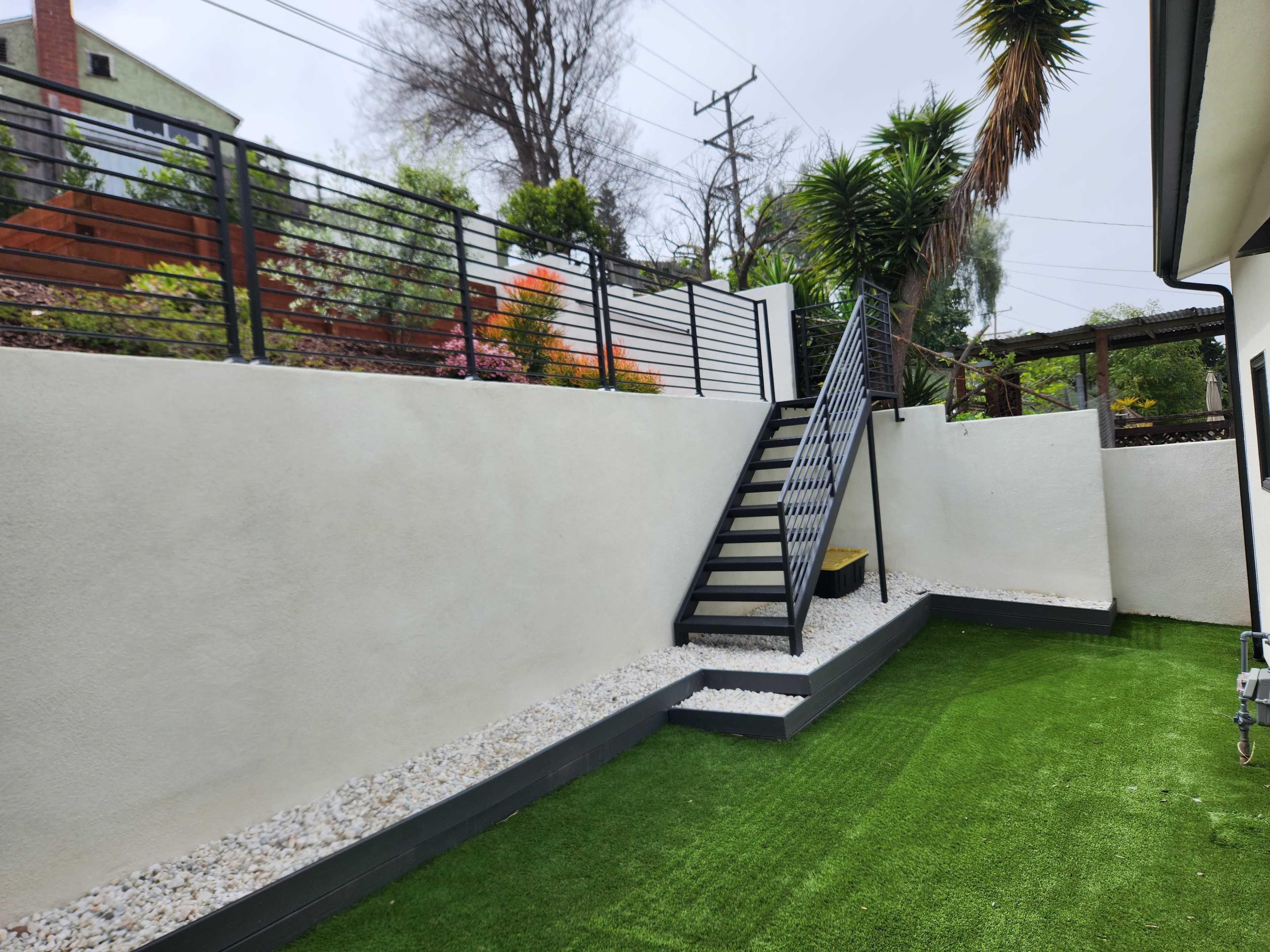 The image shows a landscaped garden with a grassy area, a staircase leading to a higher level, and a wall decorated with plants.