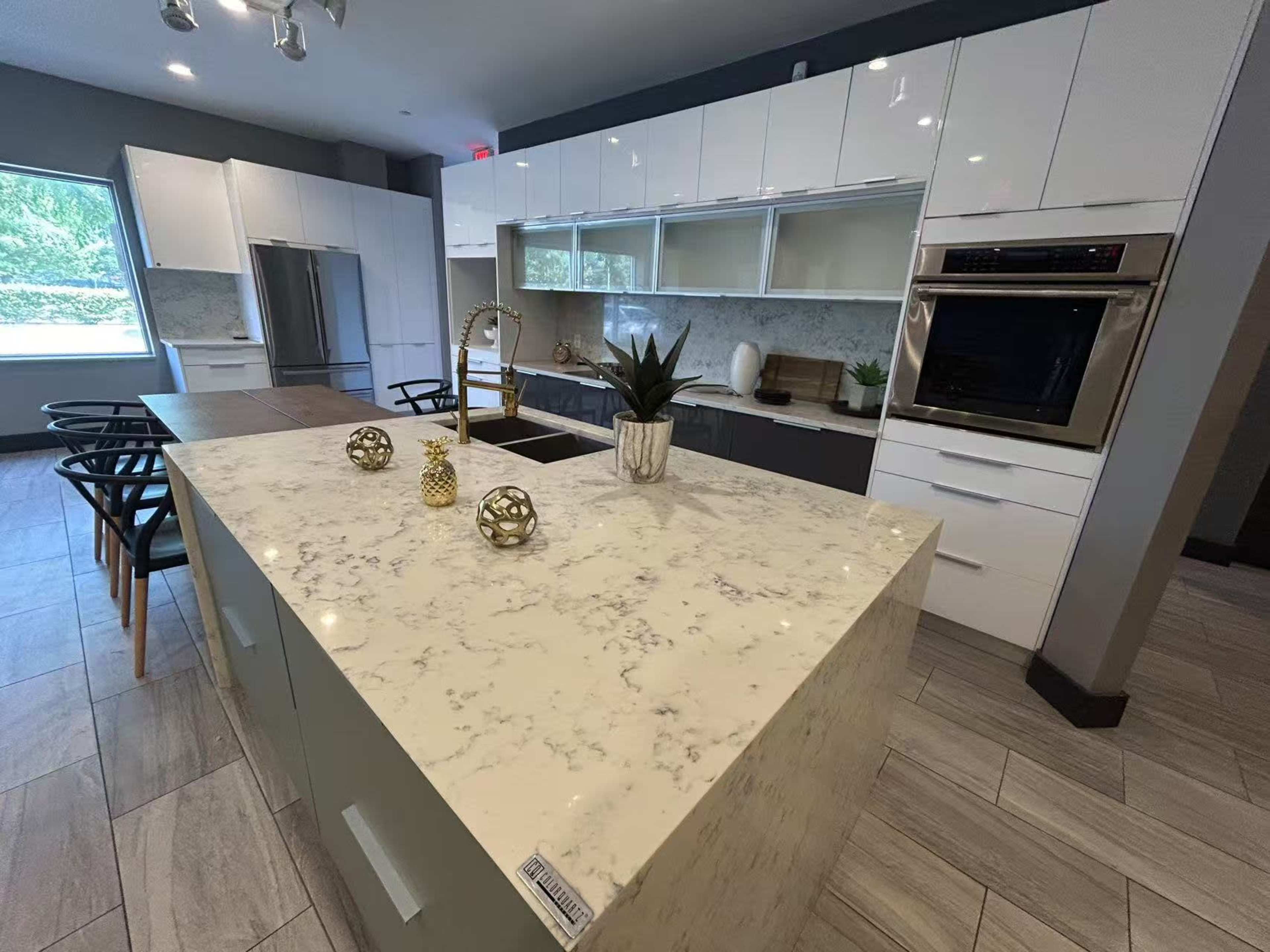 The image shows a modern kitchen featuring a marble island, sleek cabinetry, and stainless steel appliances.