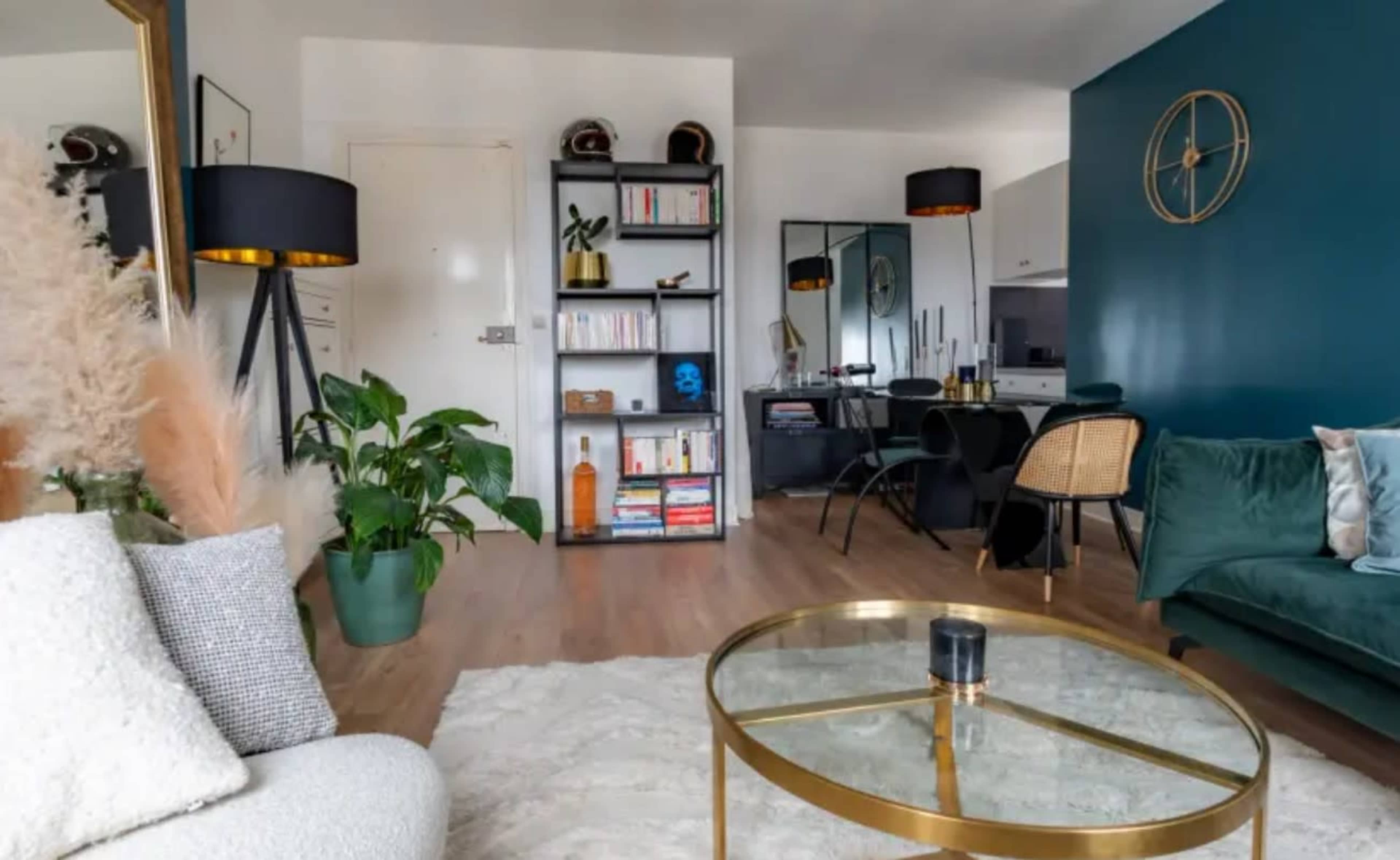 The image shows a modern living room with a green sofa, a round coffee table, a decorative plant, and a bookshelf, all set against a teal wall.