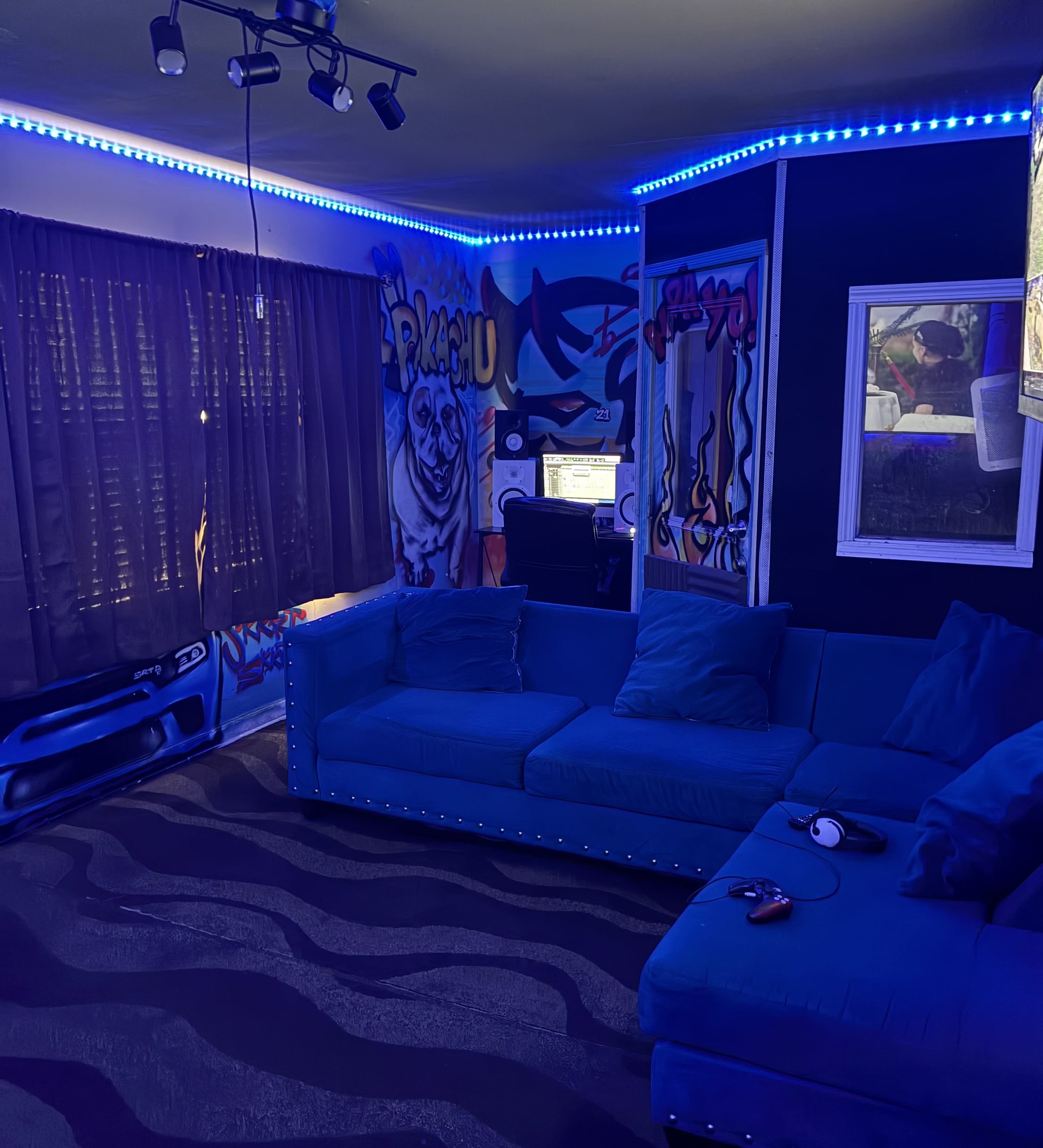 The image shows a dimly lit room with a blue couch, graffiti-covered walls, and ambient LED lighting along the ceiling.