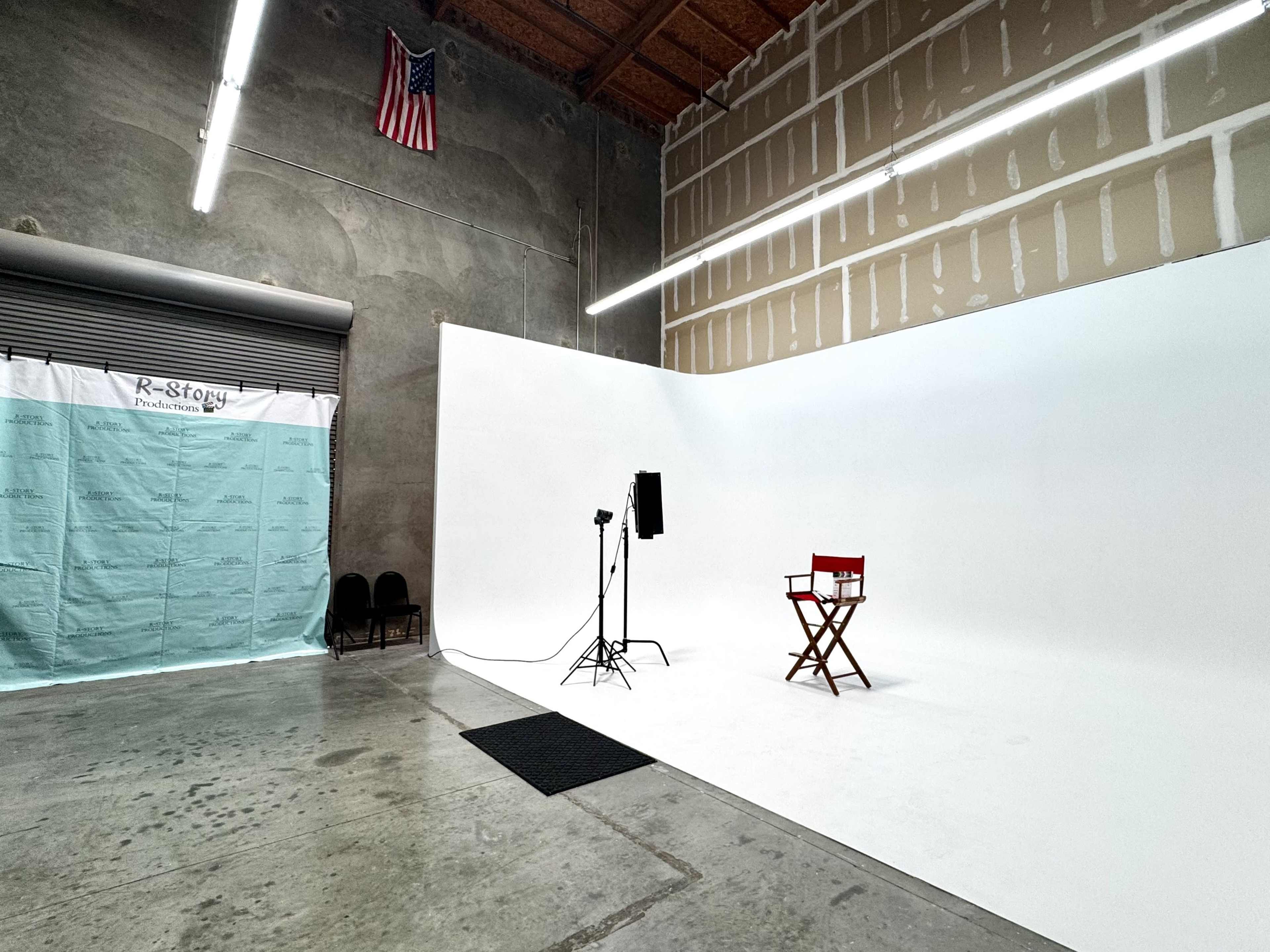 The image shows a spacious studio setup with a white backdrop, a red director's chair, a light stand, and a turquoise backdrop to the left.