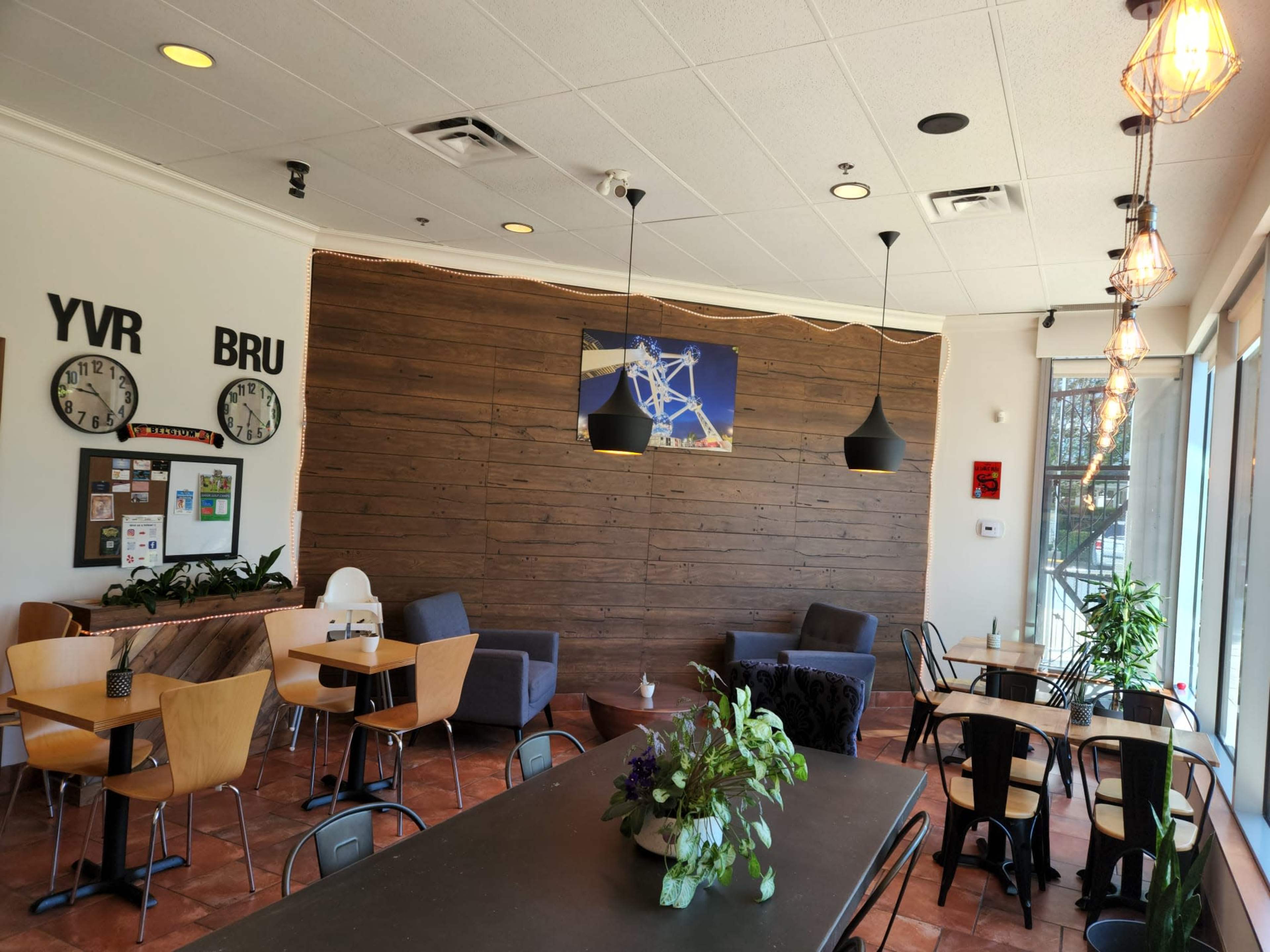 The interior of a cafe features wooden walls, a mix of seating arrangements, and large windows allowing natural light to enter.