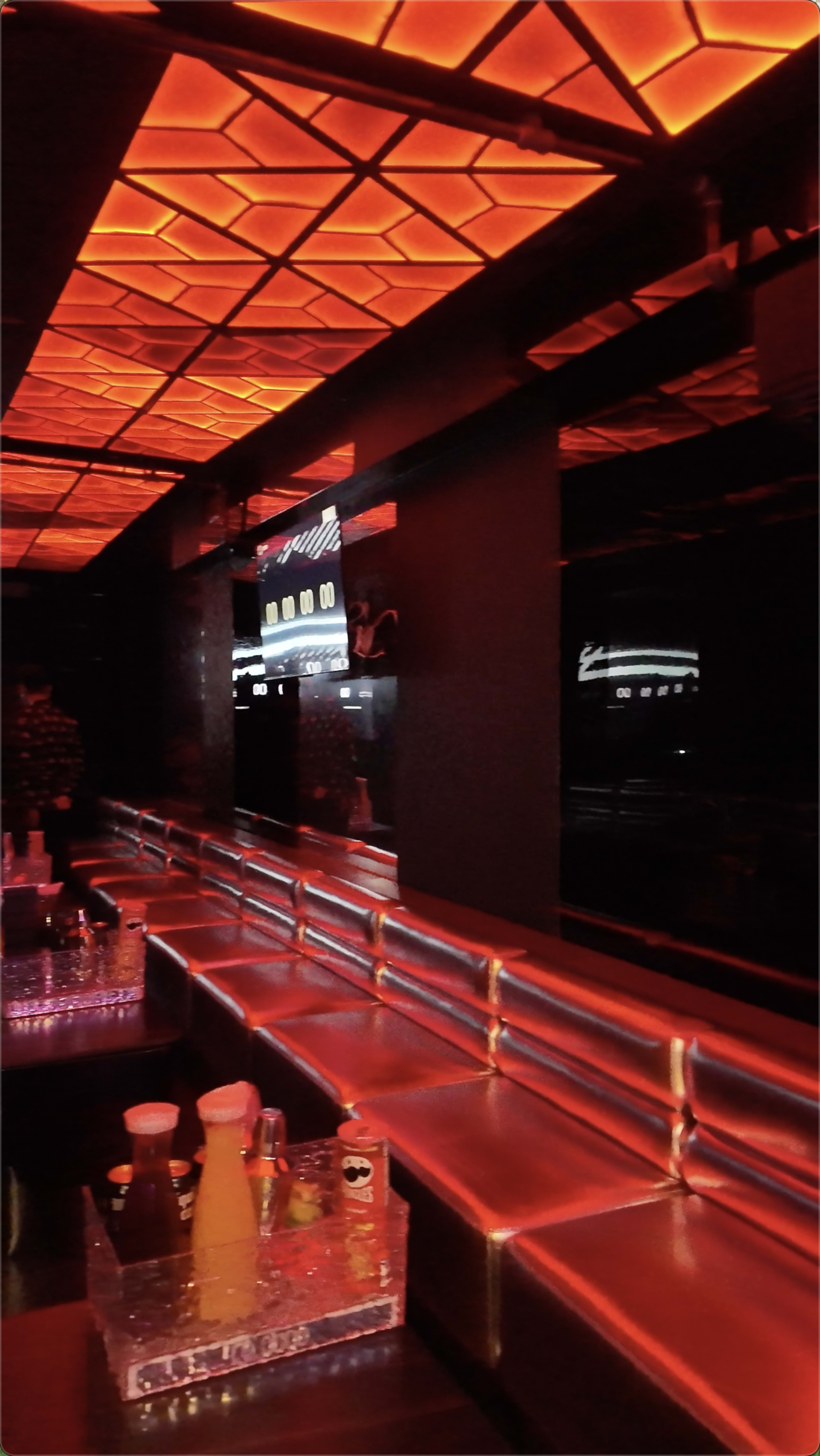 The image shows a dimly lit bar area with a glowing orange ceiling and silver seating along the counter.