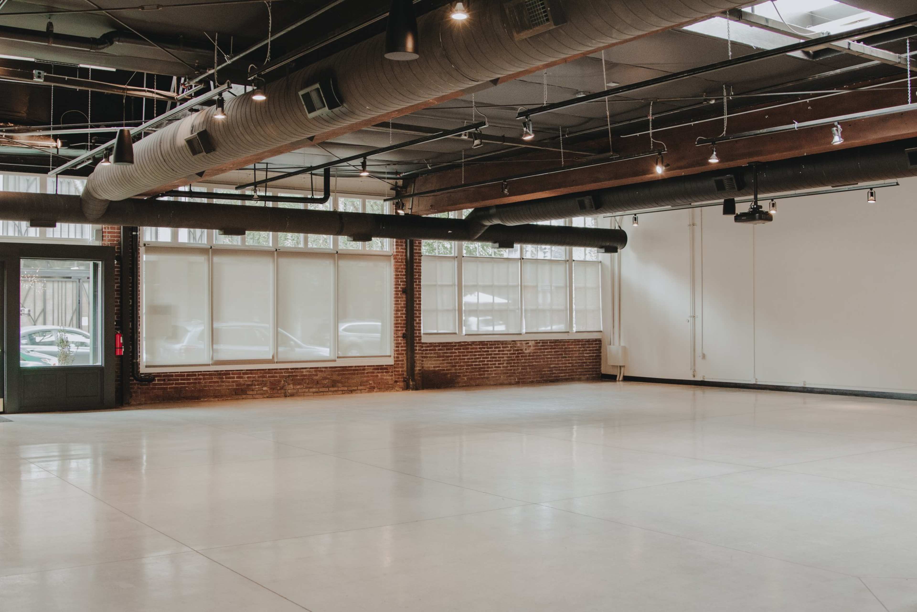 A spacious, well-lit room with large windows, exposed brick walls, and a polished concrete floor.