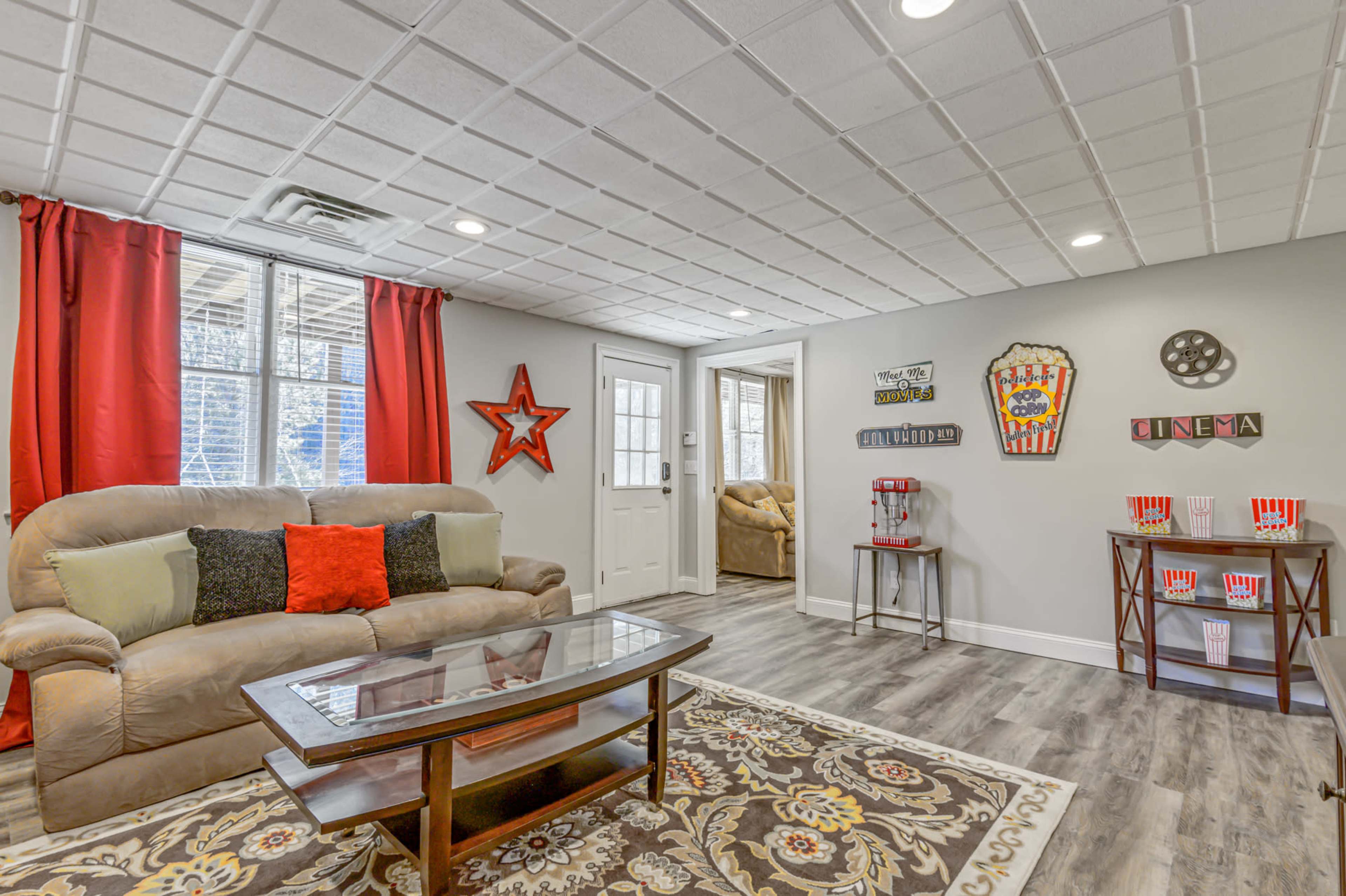 The room features a brown sofa with decorative pillows, a coffee table, and red curtains, alongside a movie-themed decor including a popcorn stand and vintage cinema signs.