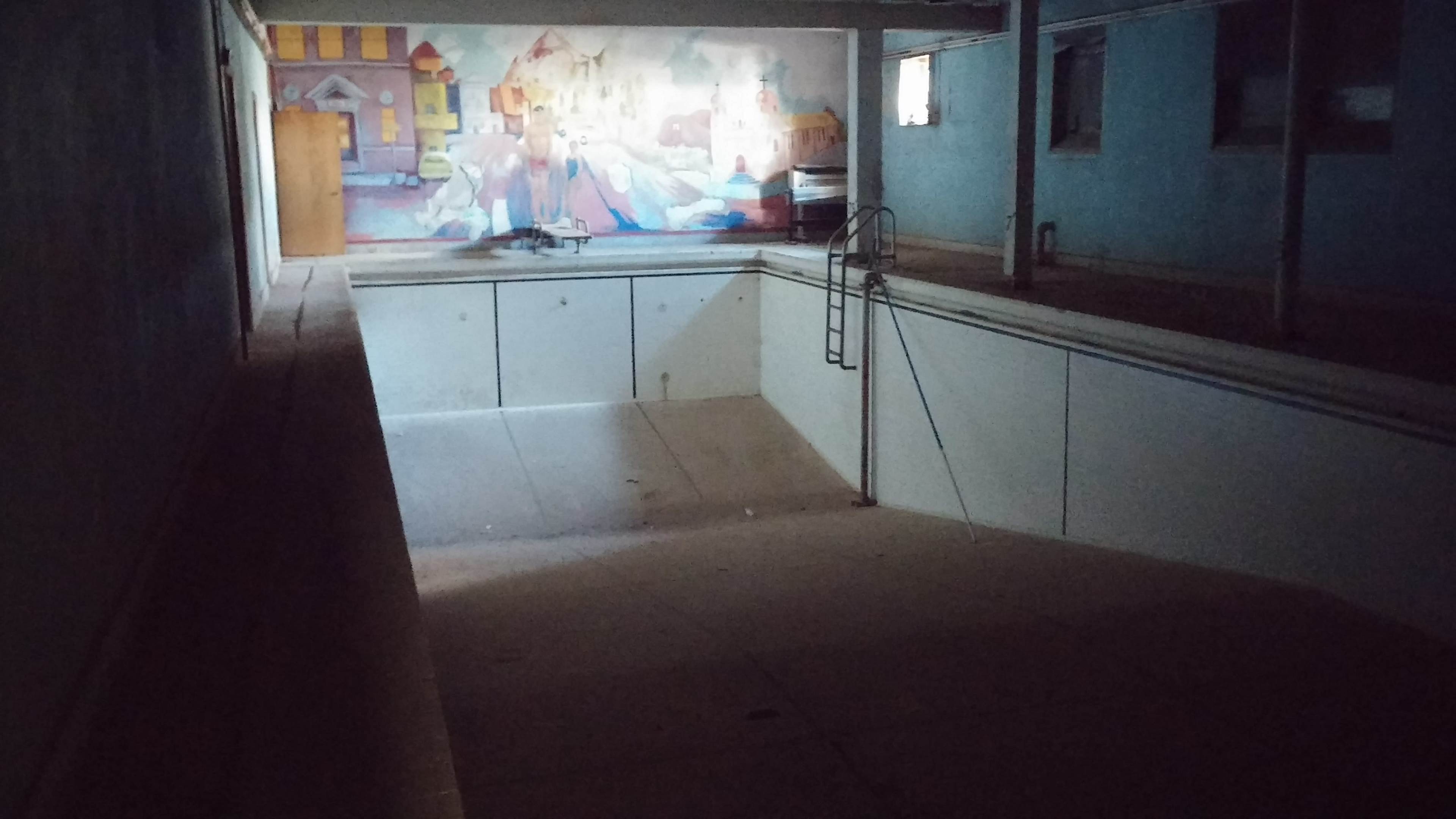 An empty indoor swimming pool with a mural depicting a cityscape on the wall in the background.