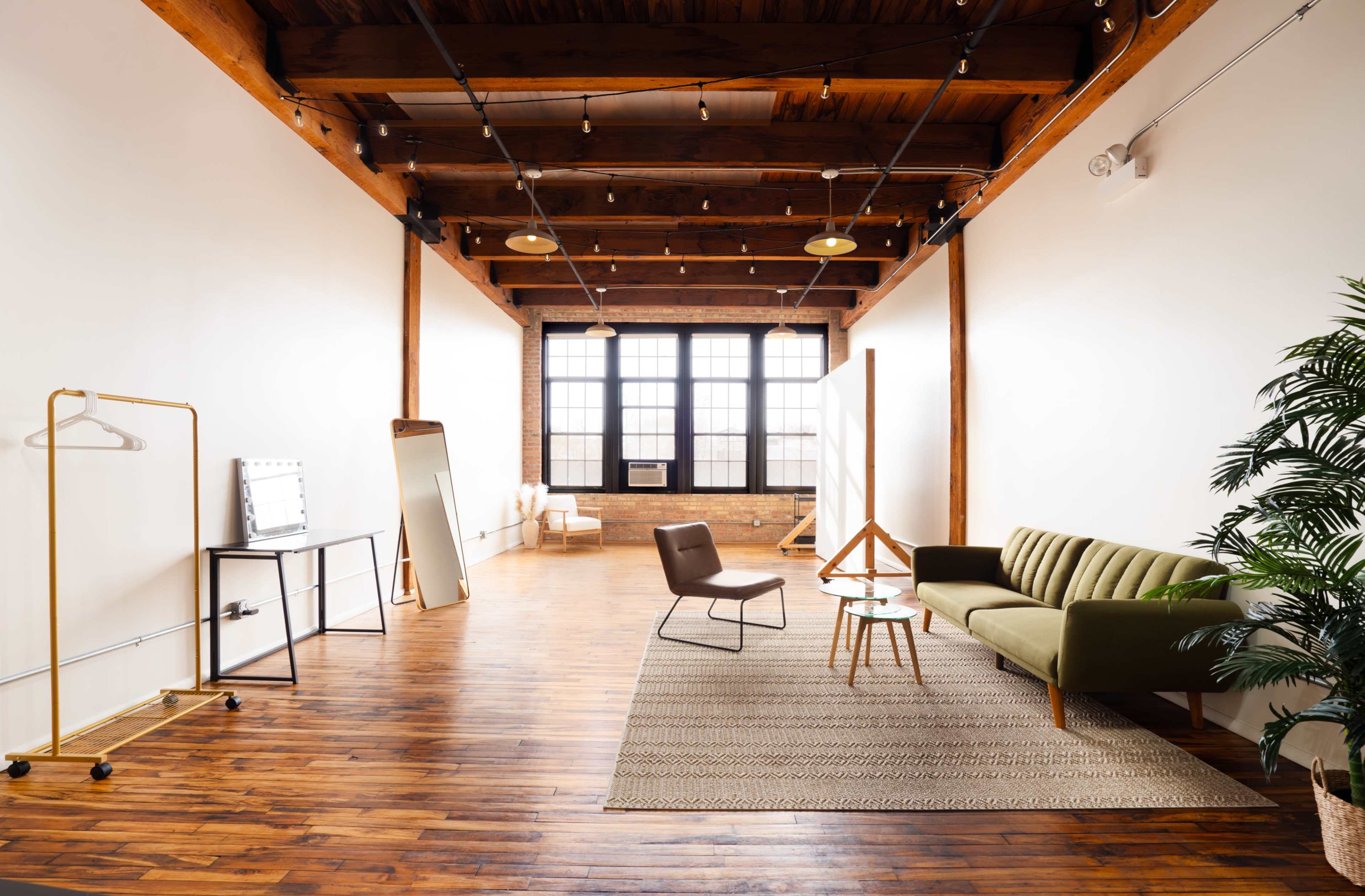A spacious, modern room featuring wooden beams, a green sofa, a coffee table, and a large window.
