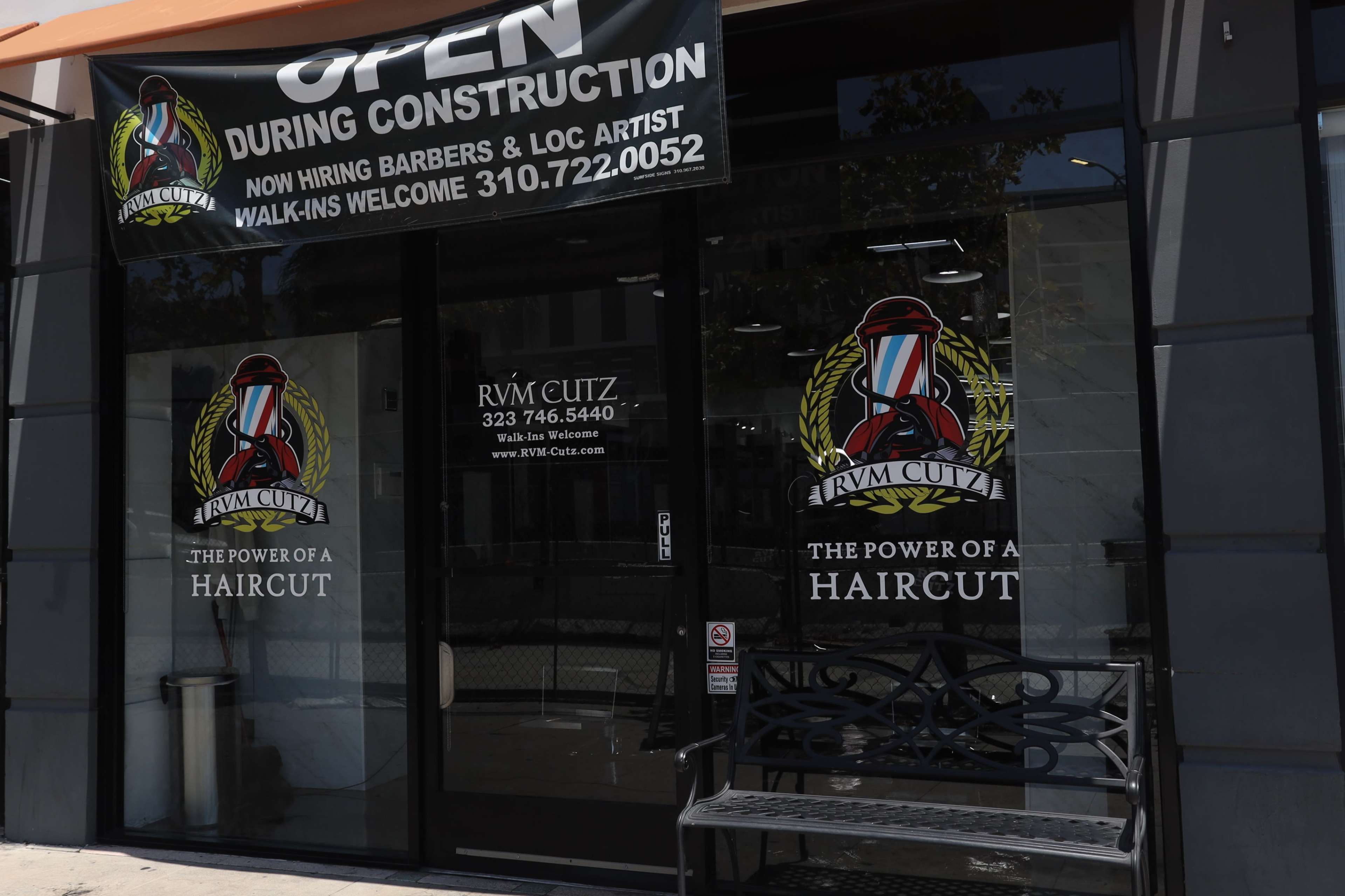 A barbershop with a sign indicating it is open during construction and features a logo with a barber's pole.