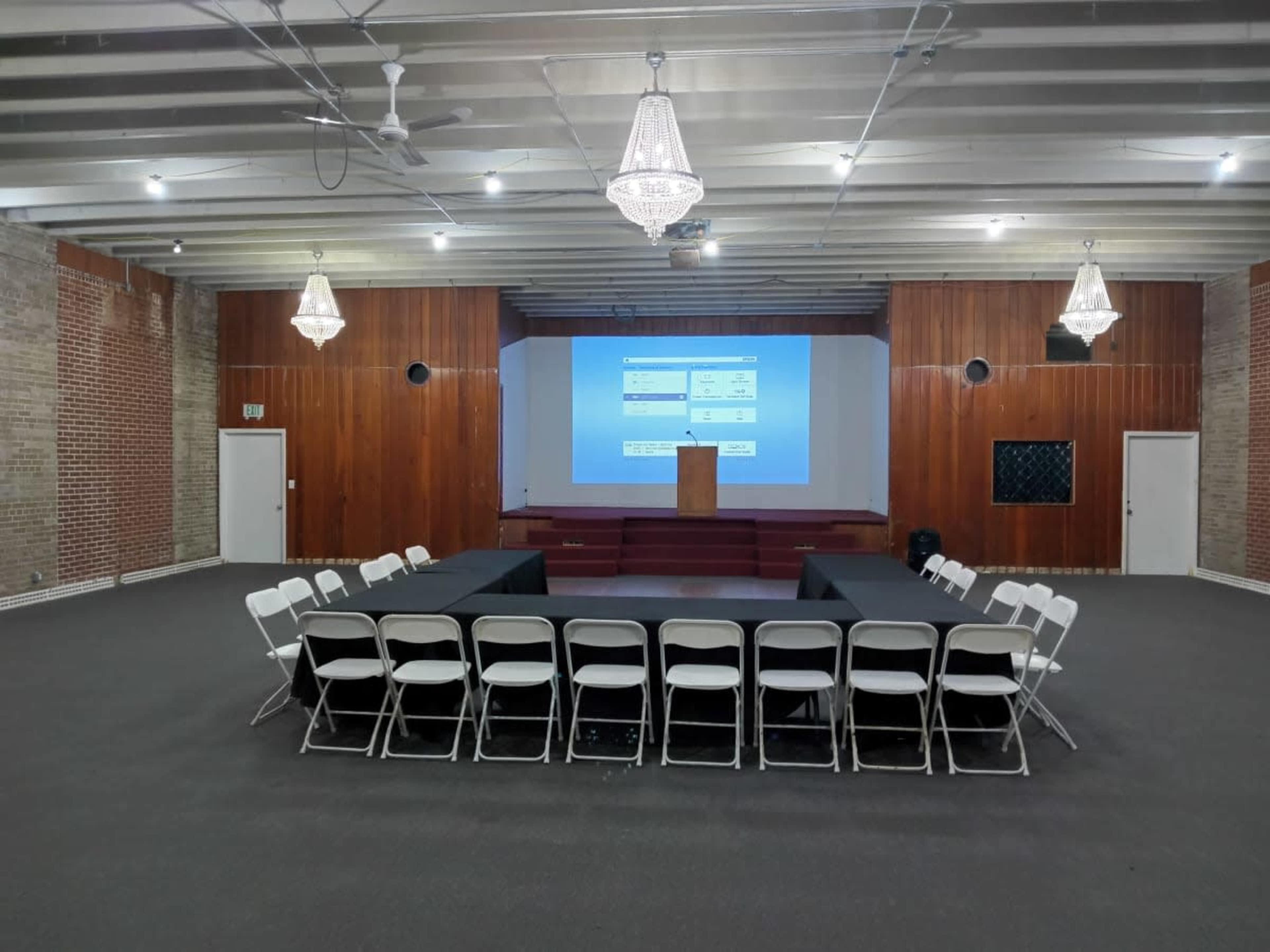 A large room is set up for a conference, featuring a central arrangement of chairs surrounding a podium and a projection screen.