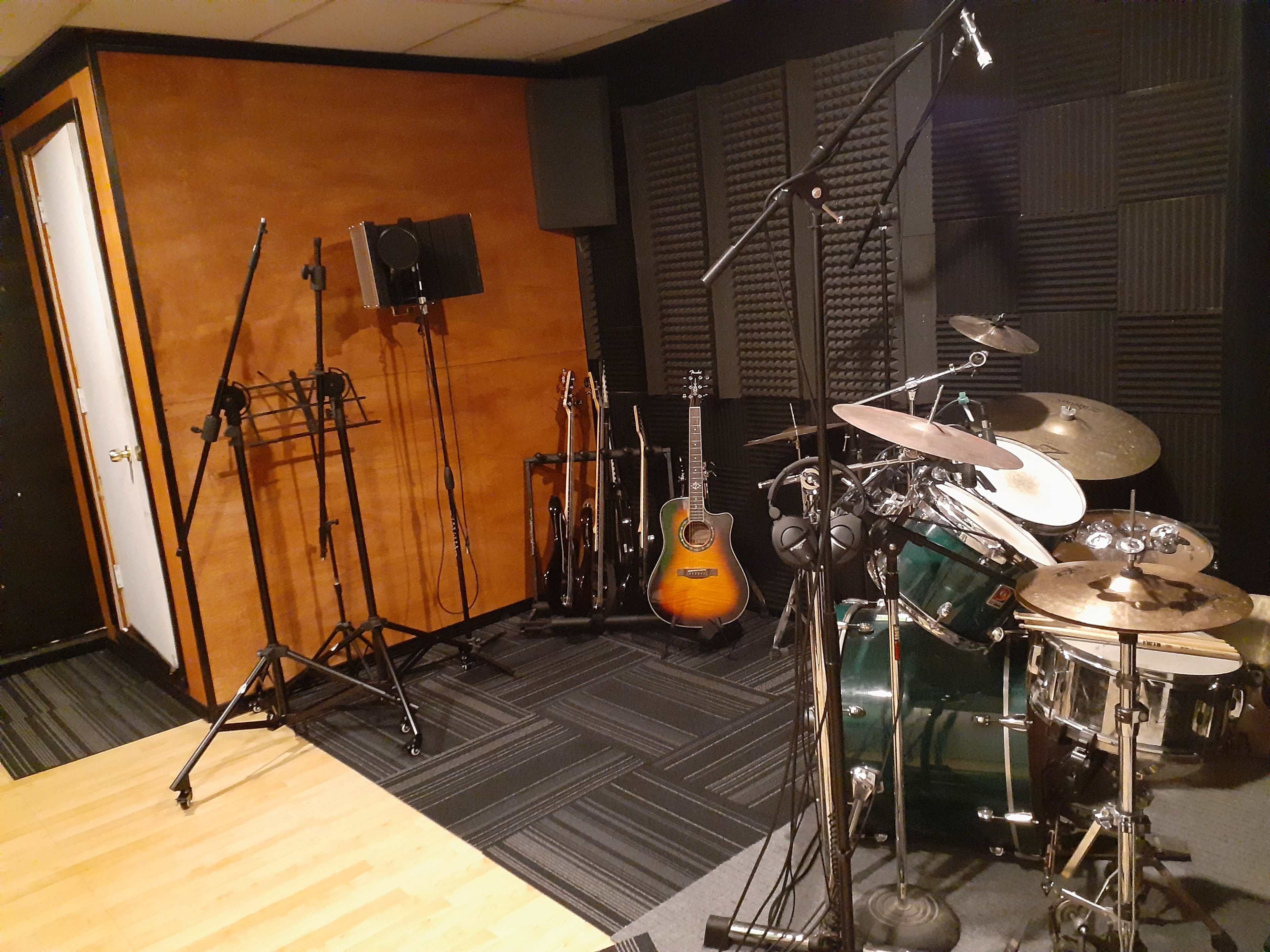 A music recording studio featuring a drum set, several guitars on stands, and soundproofed walls.