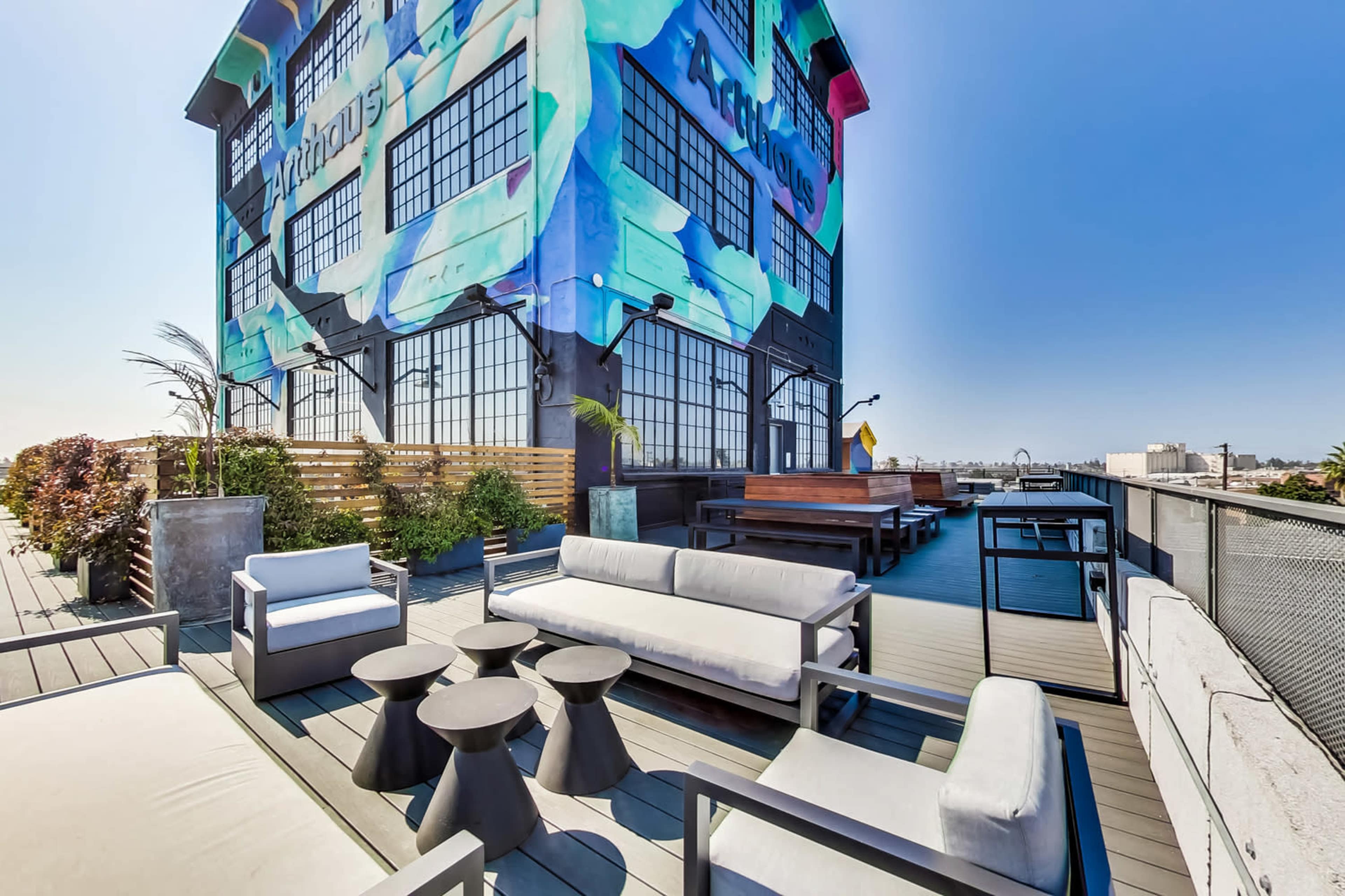 A rooftop terrace featuring modern seating arrangements and a vibrant mural on the side of a building.