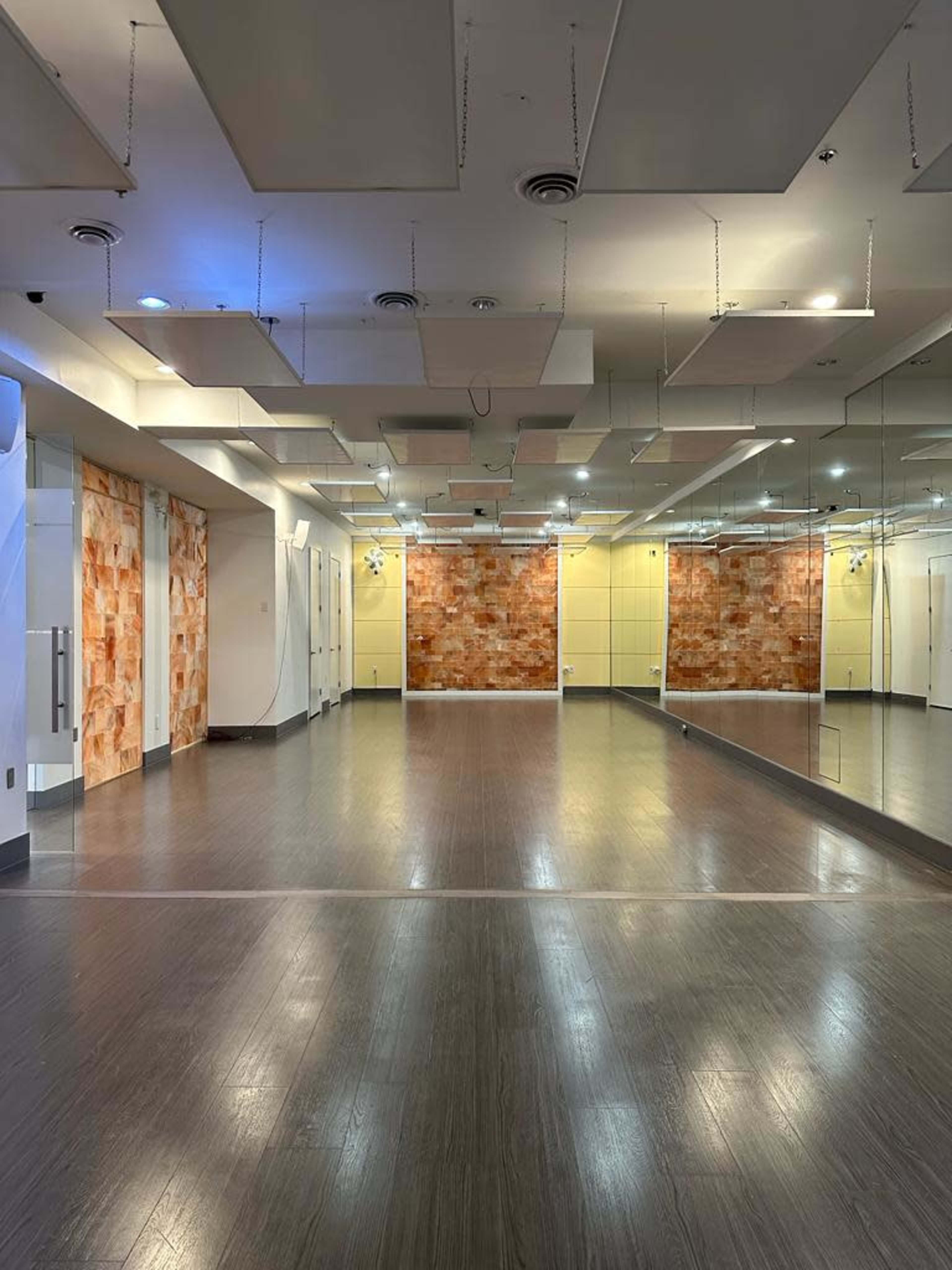 A spacious dance studio with mirrored walls and wooden flooring, featuring textured panels on one side.