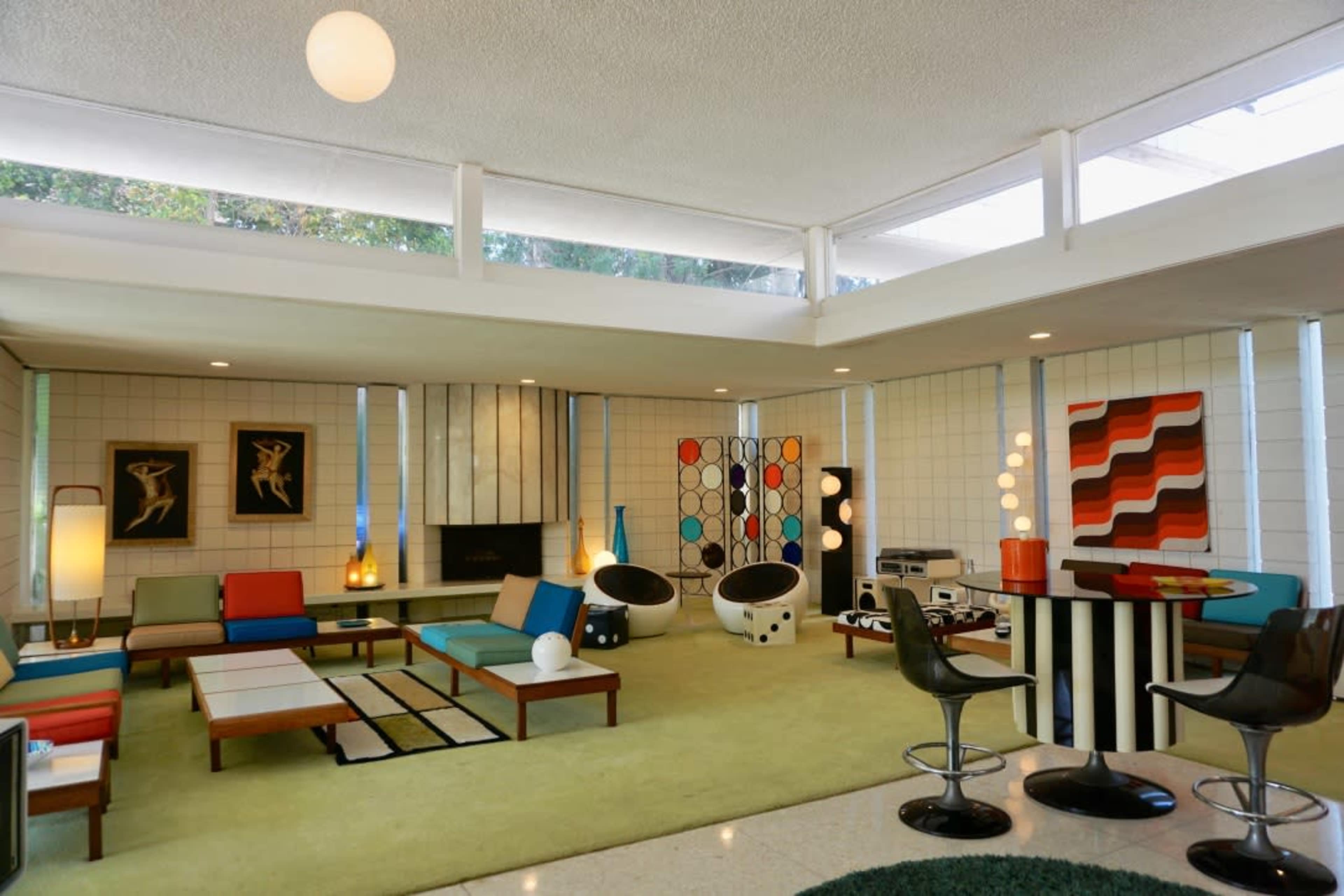 A mid-century modern living room featuring colorful furniture, geometric artwork, and large windows that bring in natural light.