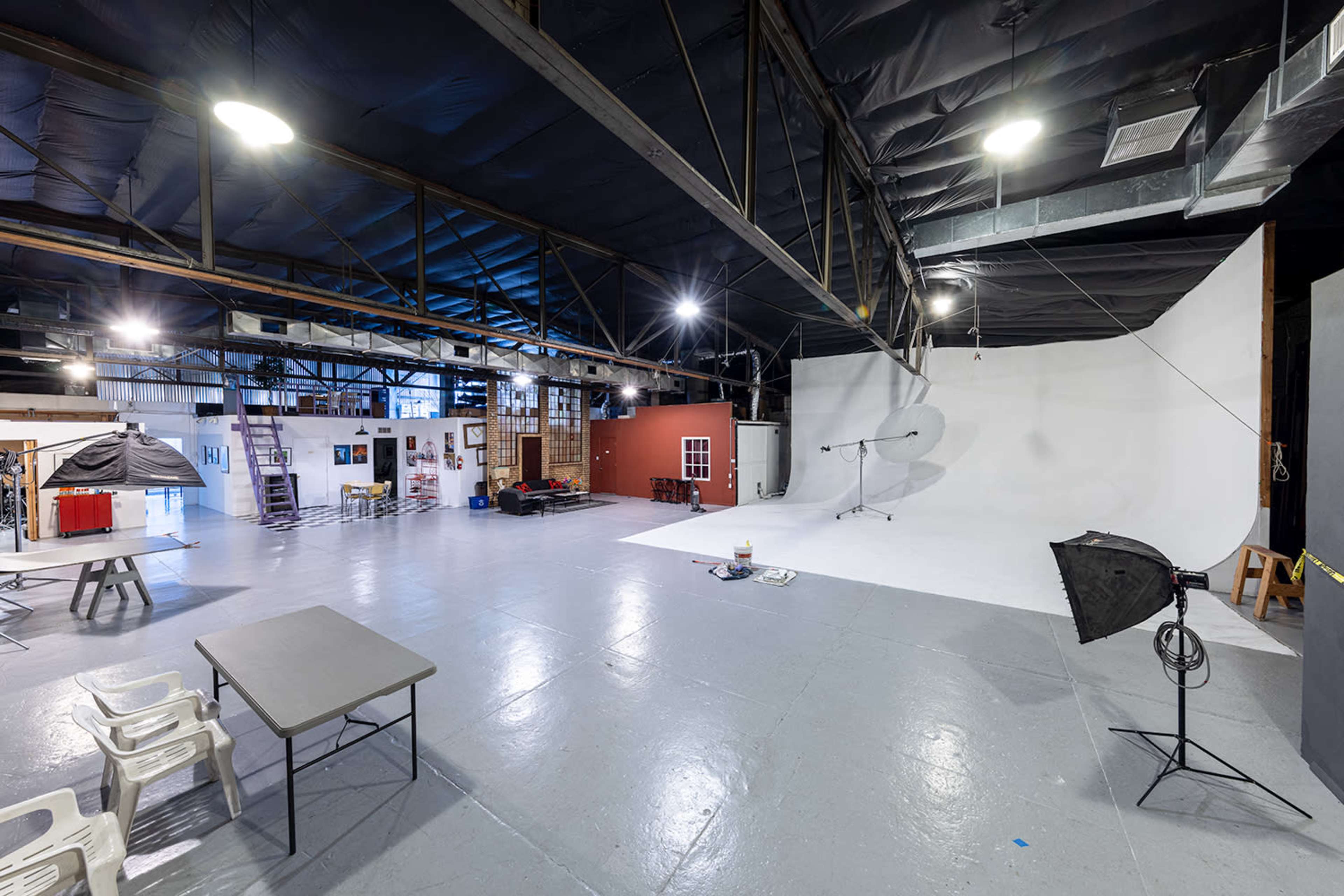 A spacious photography studio with a large white backdrop, various equipment, and multiple seating areas.