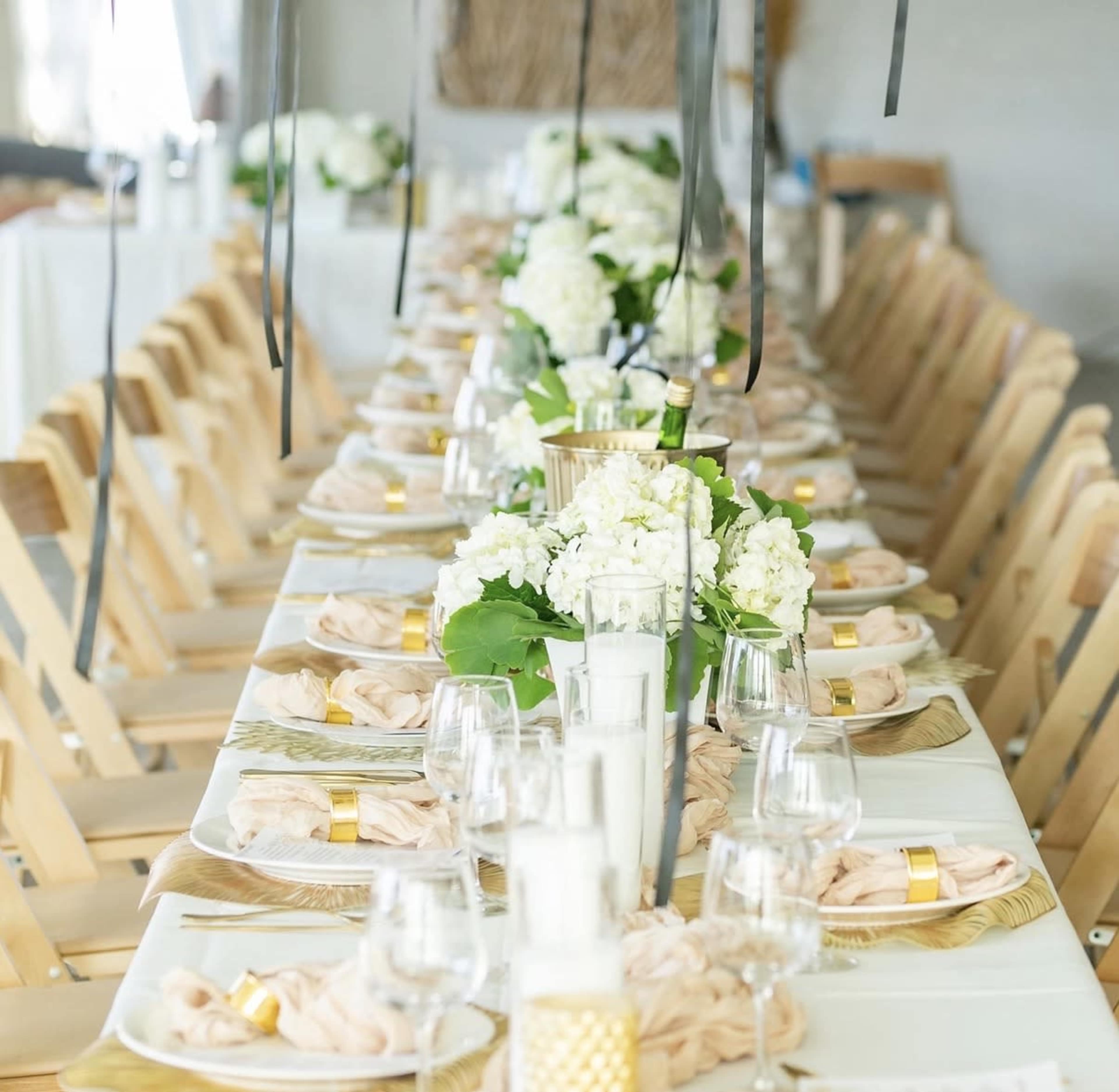 A long dining table is set with white plates, glasses, and floral centerpieces, surrounded by wooden chairs.