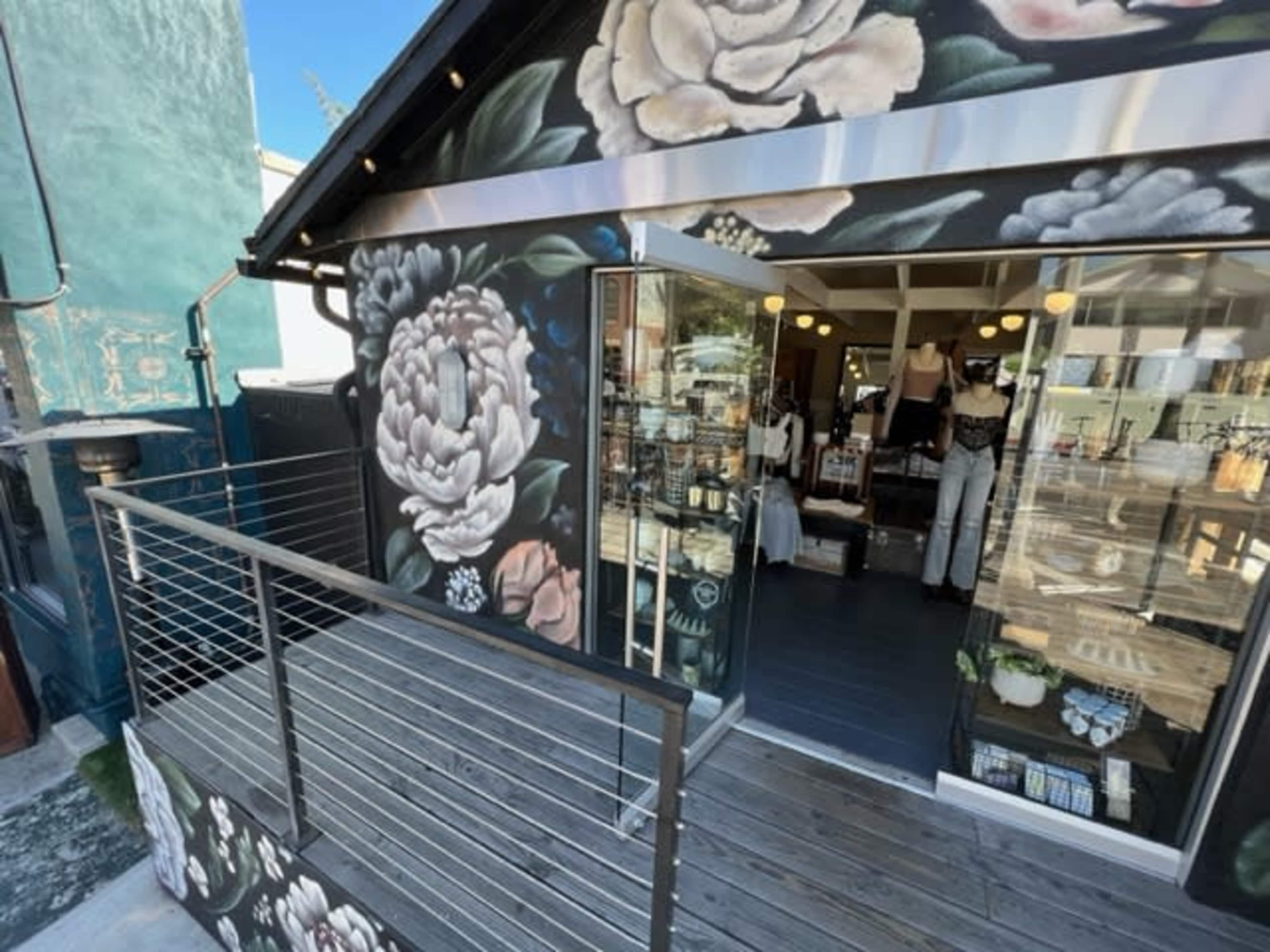 The image shows a boutique with large floral murals on its exterior, featuring a glass entrance and a wooden deck.