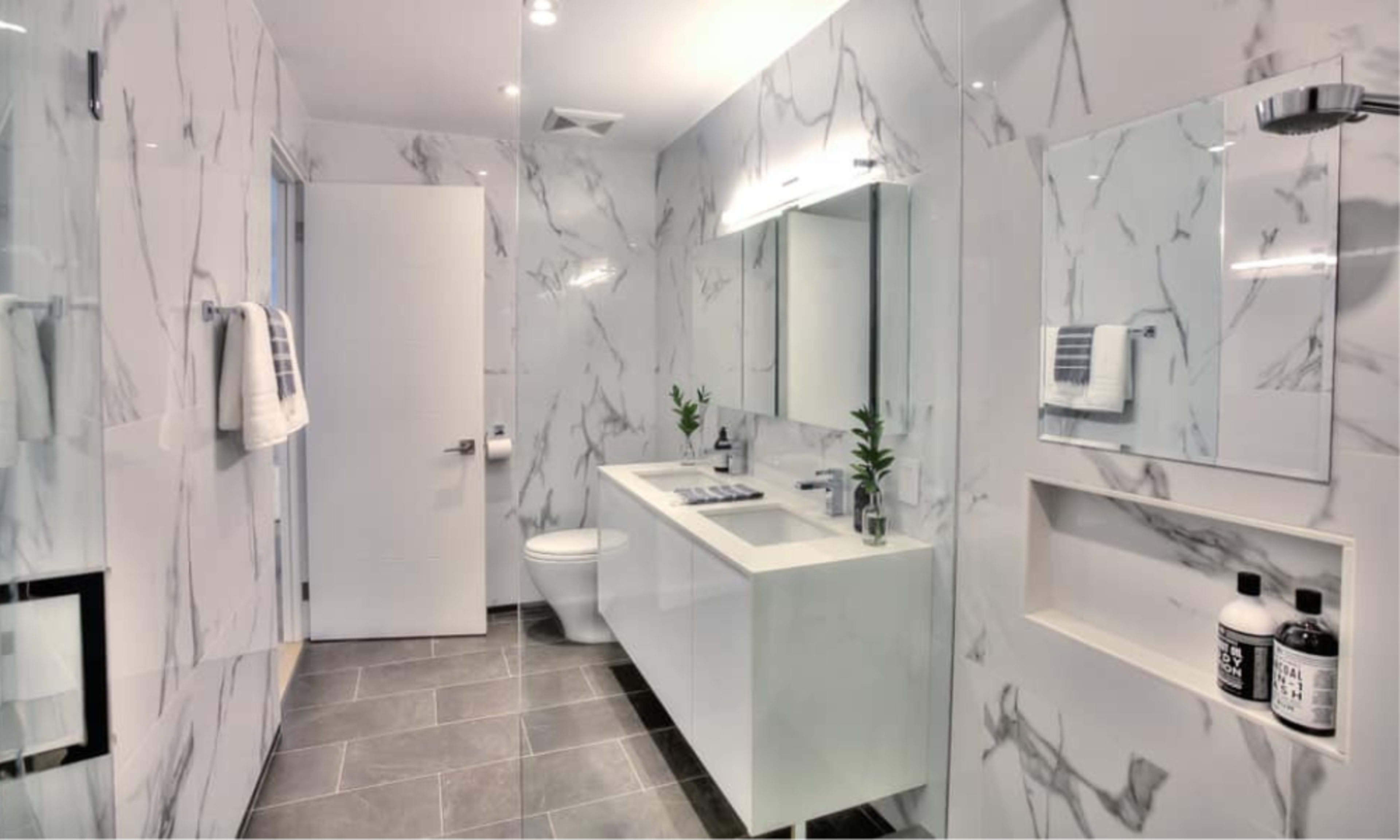 A modern bathroom with marble walls, a white vanity, and a clean, organized layout.