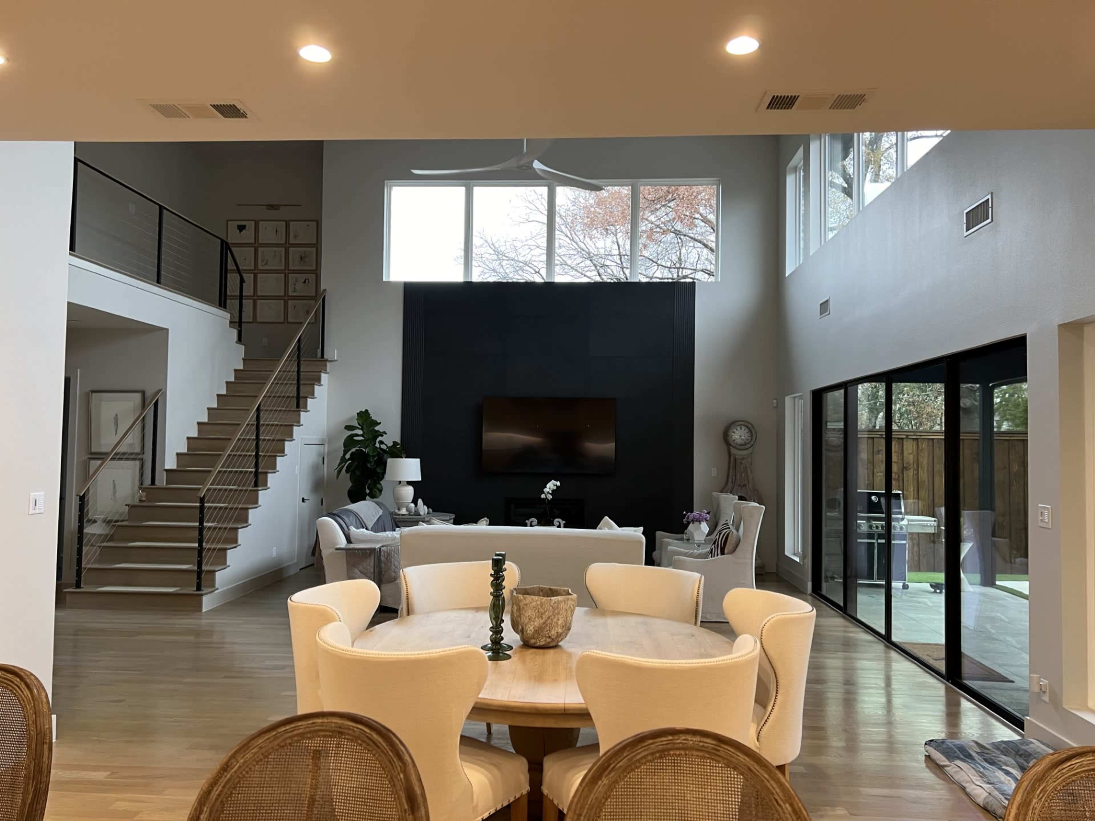 A spacious, modern living area with a view of a staircase, a large television on a black wall, and glass doors leading to an outdoor space.