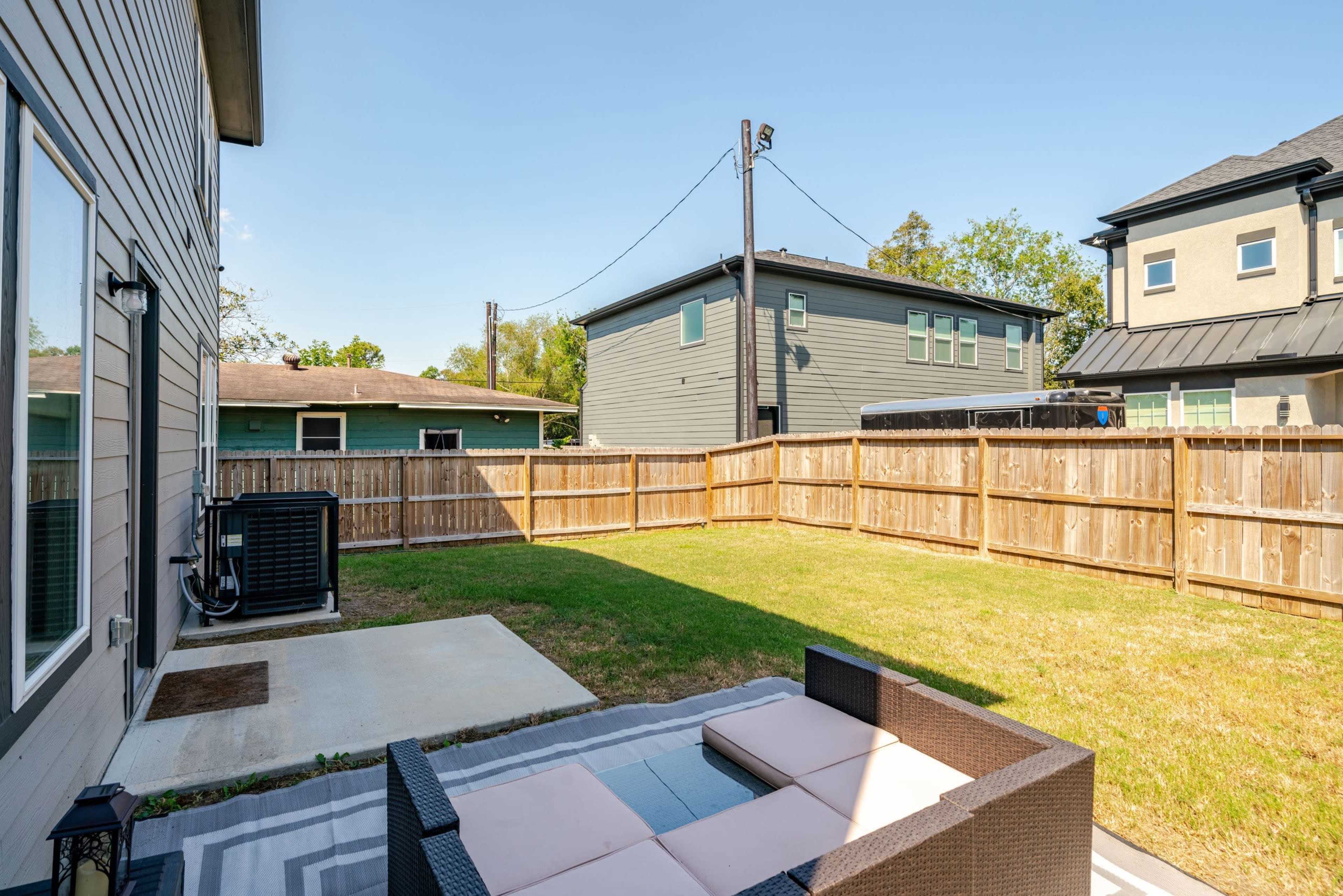 The image shows a backyard with a fenced area featuring a small patio set and grass, surrounded by two houses.