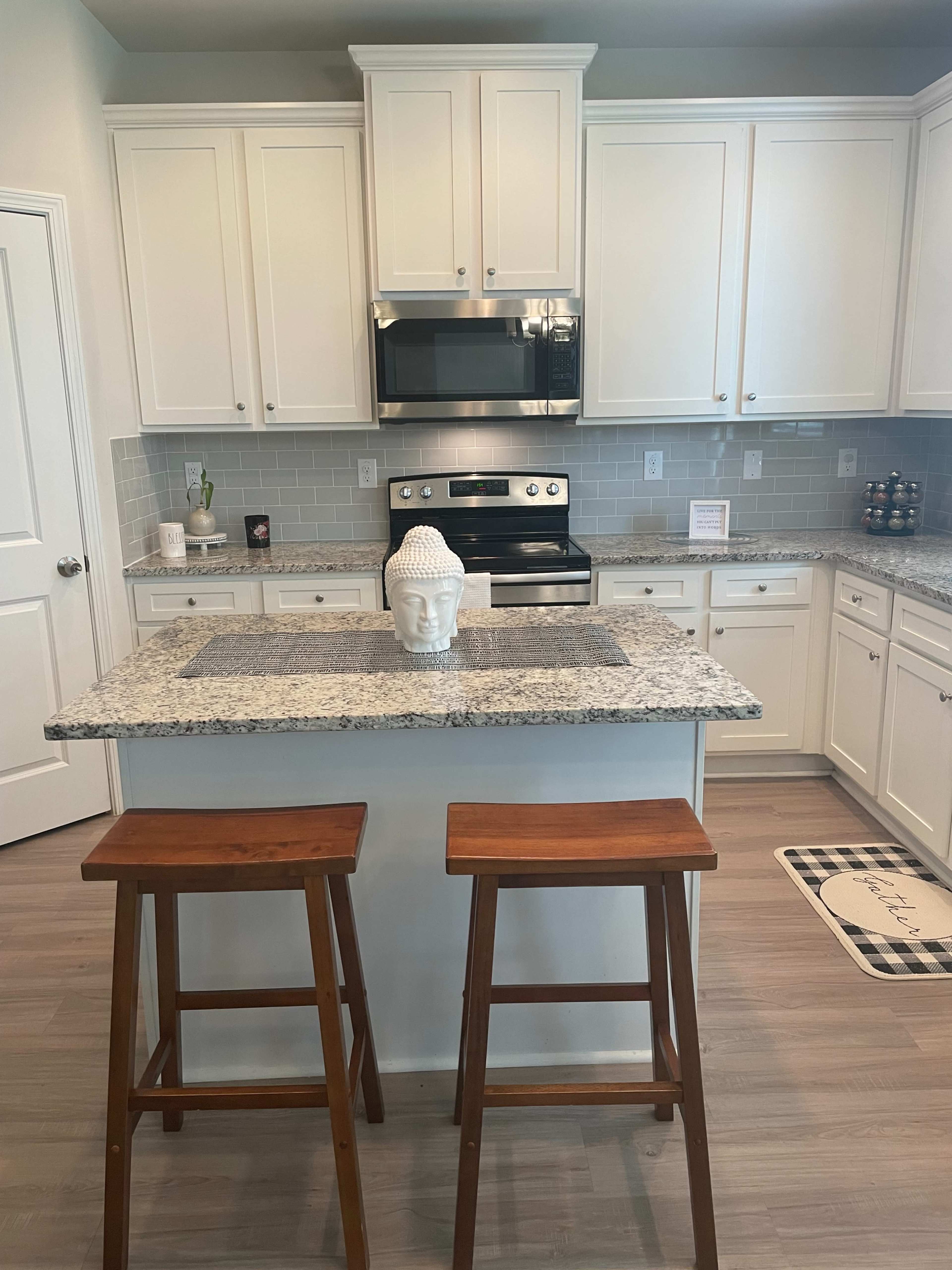 A modern kitchen features white cabinets, stainless steel appliances, a granite countertop island, and two wooden stools.