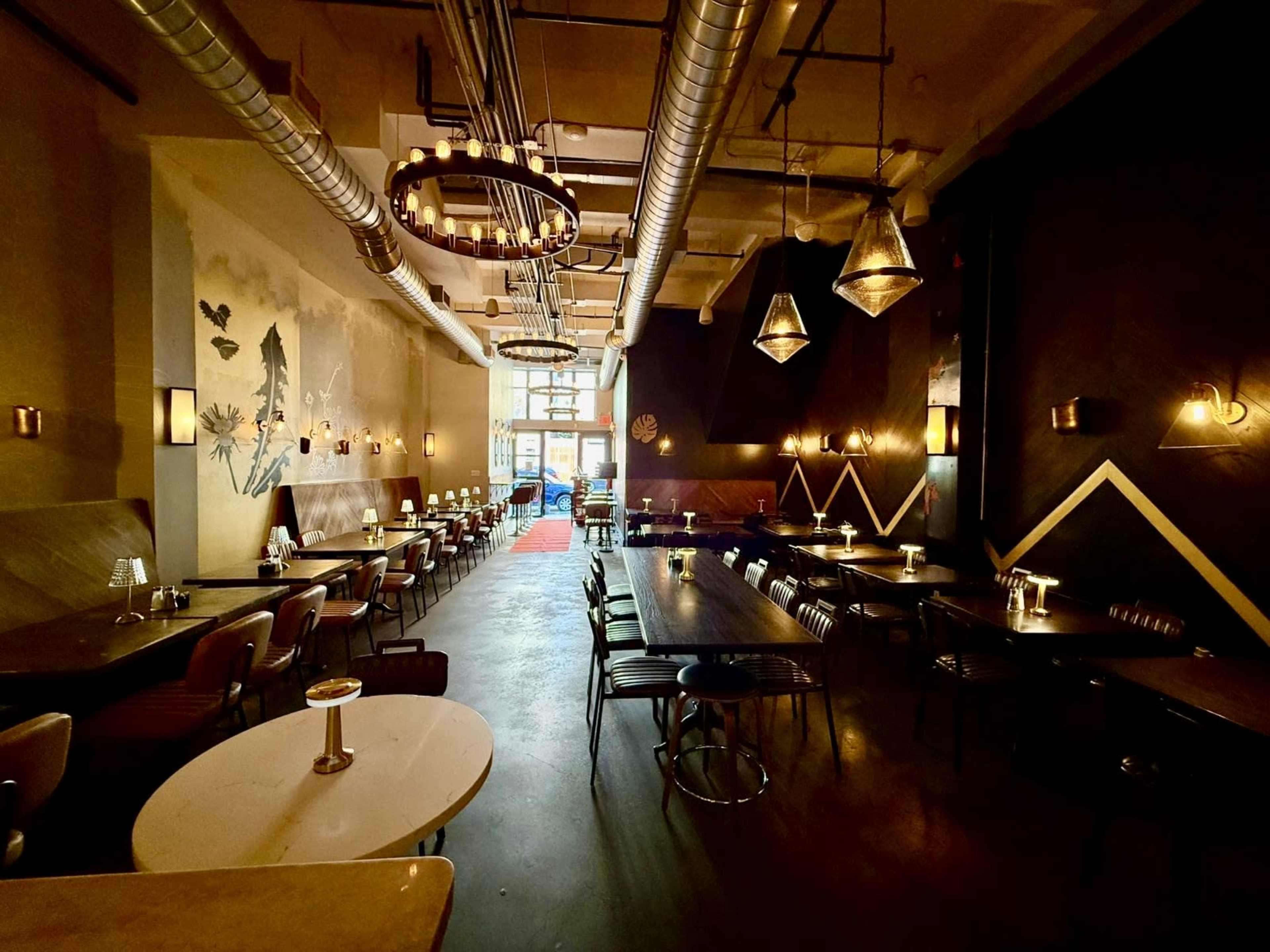 The image shows a modern restaurant with rows of tables, pendant lighting, and large windows at one end.