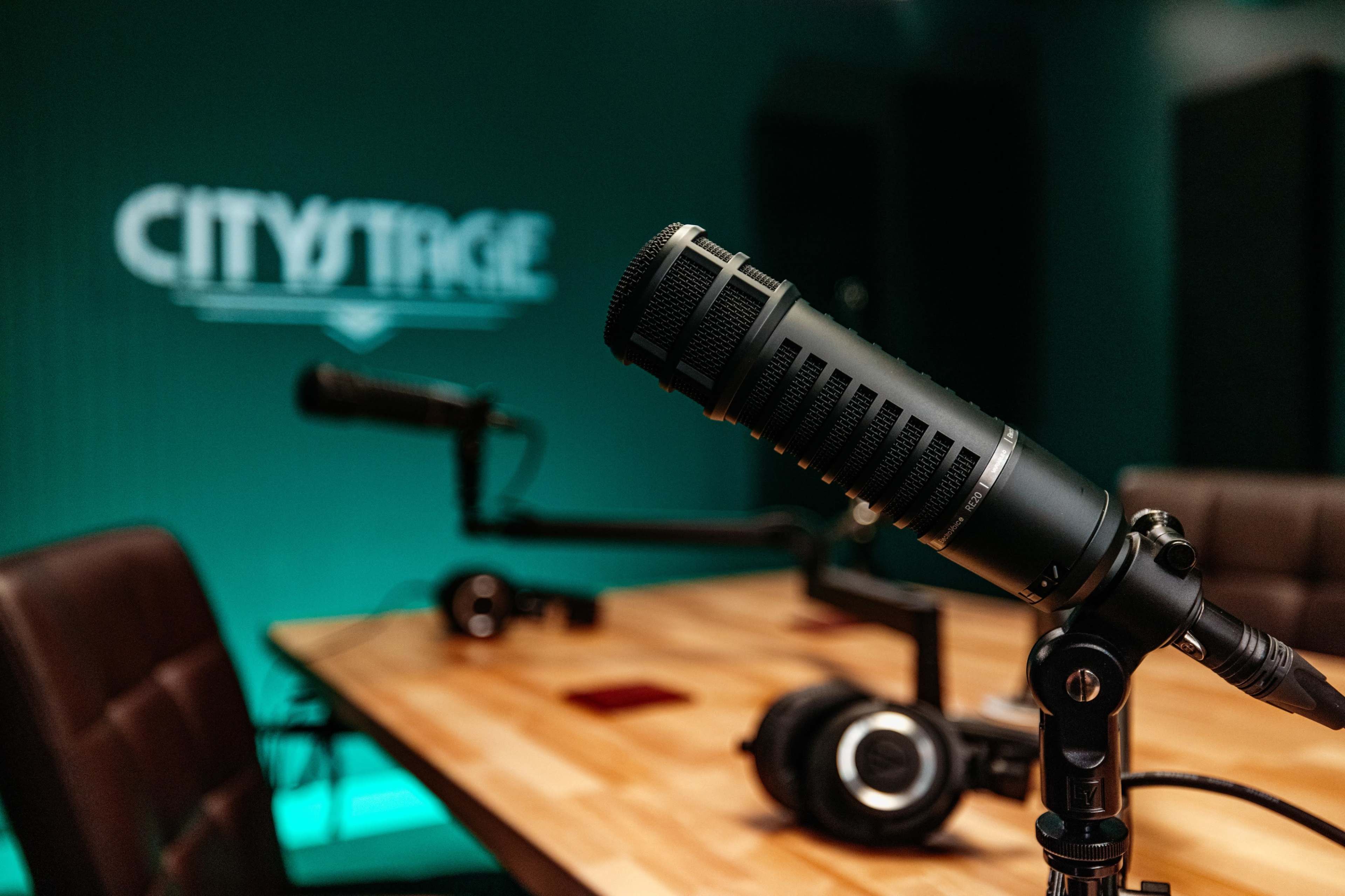 A close-up of a microphone set on a table in a recording studio with a green backdrop featuring the word "CITYSTAGE."