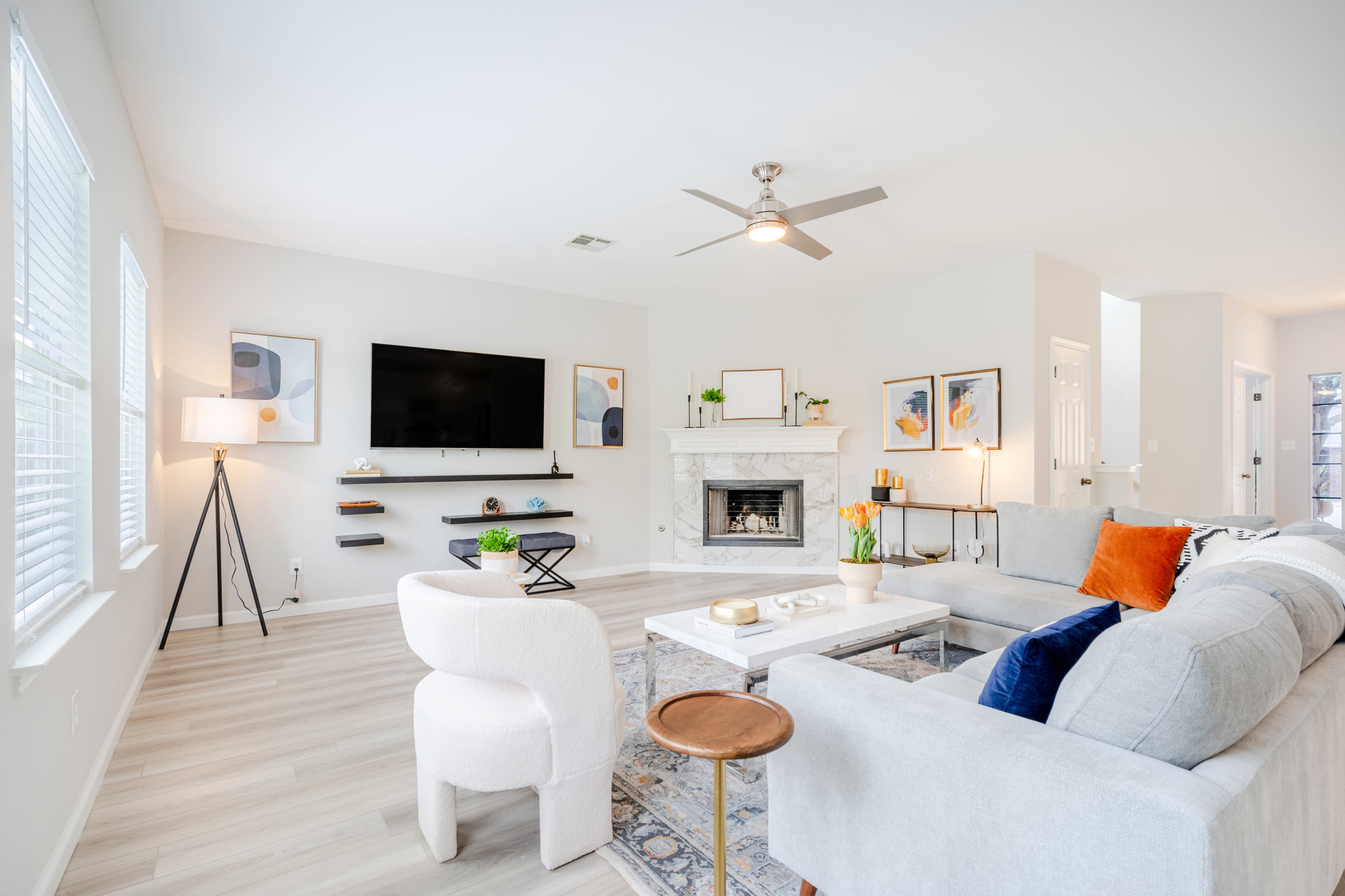 The living room features a neutral color palette with a modern sofa, a wall-mounted television, a fireplace, and artwork.
