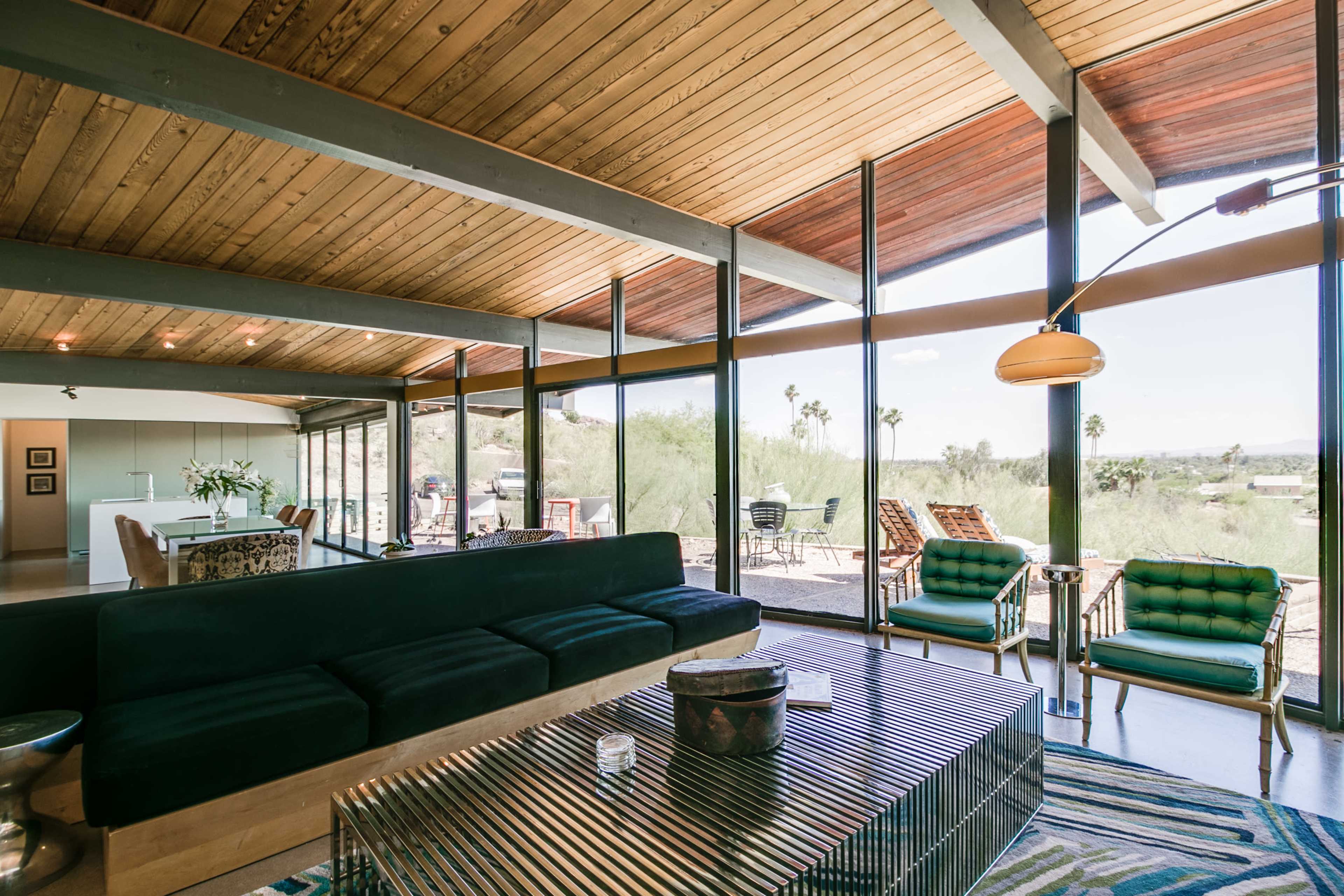 A mid-century modern living room with large windows, a green sofa, and metal accents, overlooking a desert landscape.