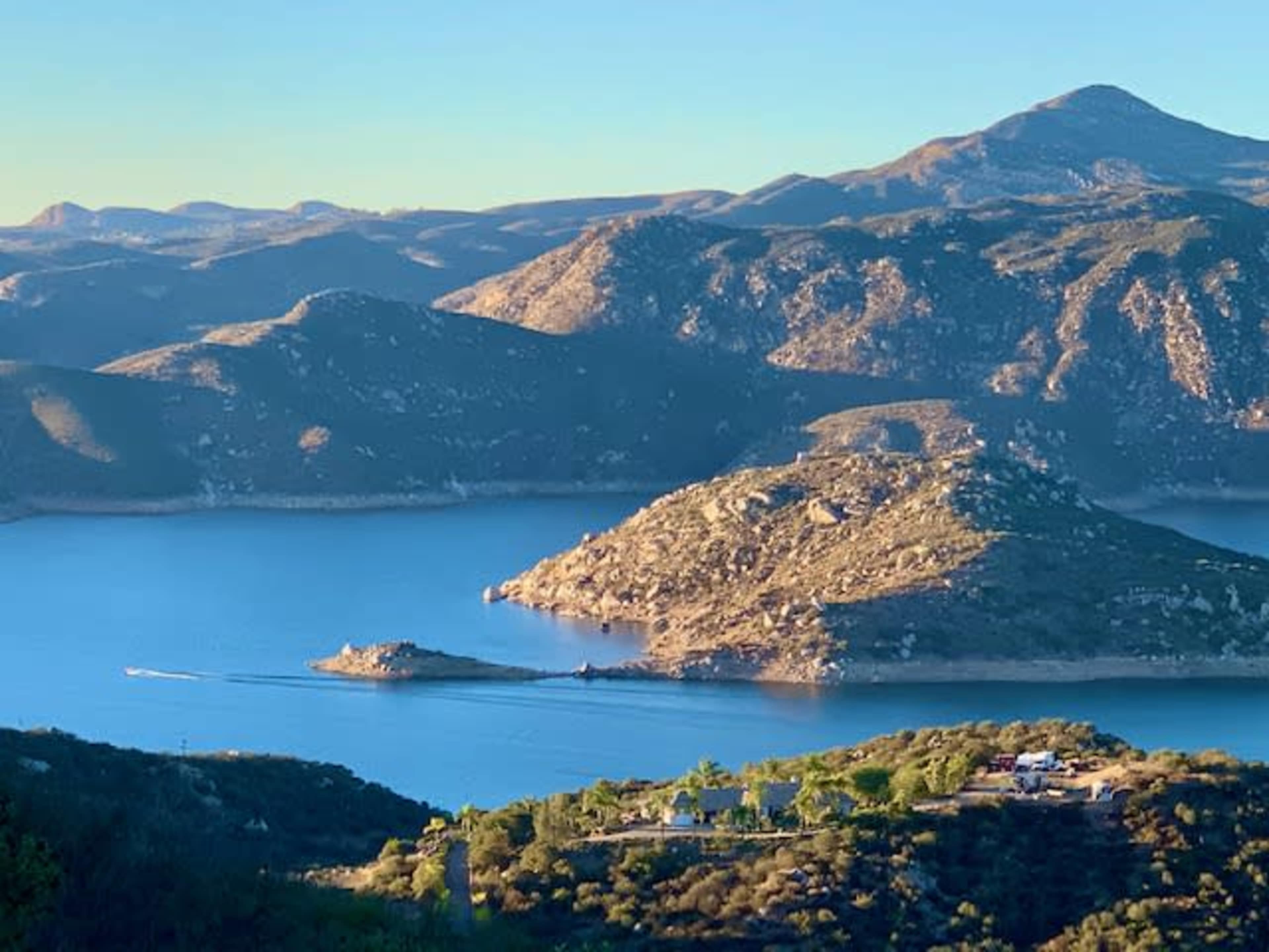 A scenic lake surrounded by hills, with a small island in the center and a boat navigating the water.