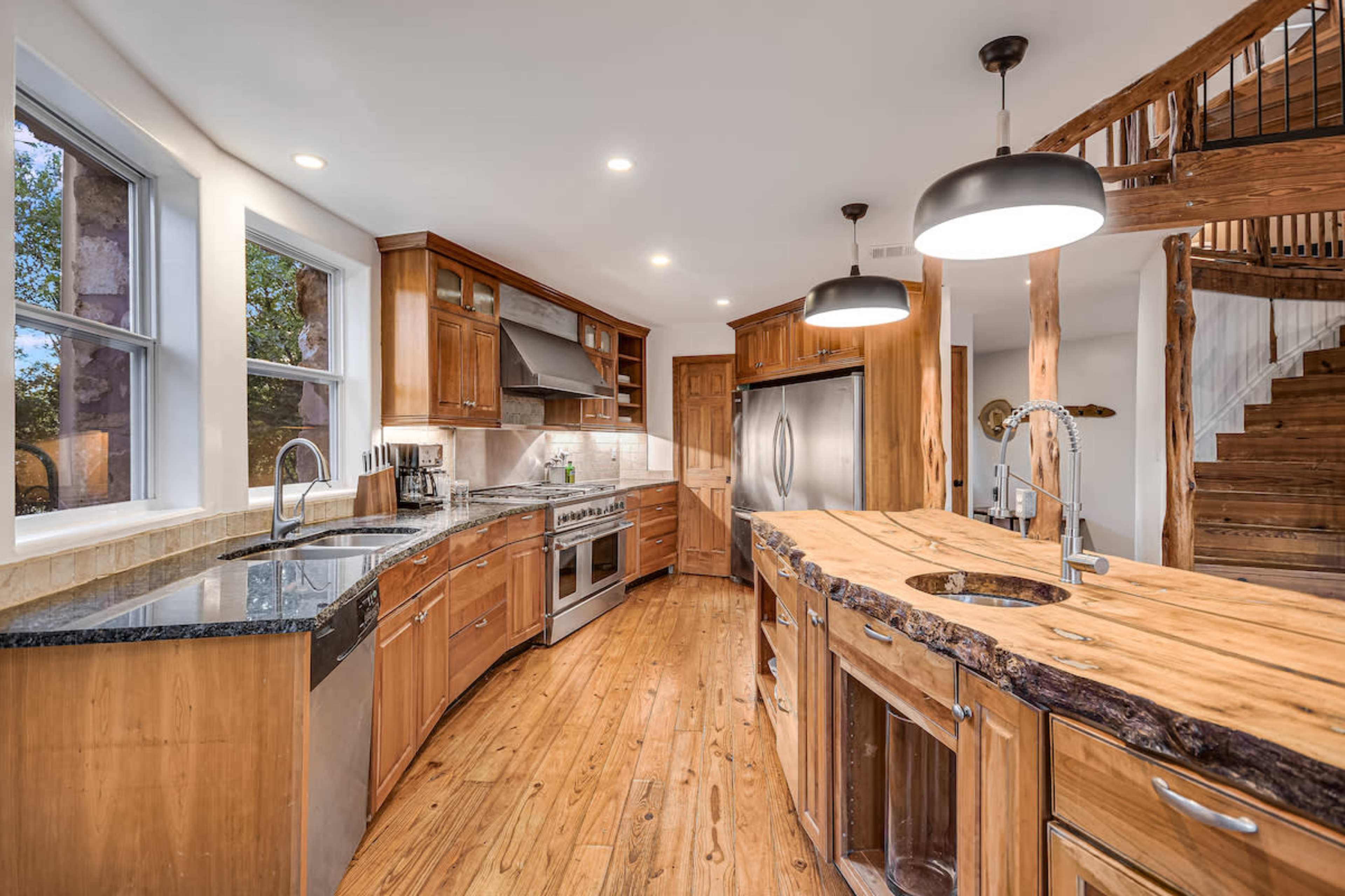 A modern kitchen featuring wooden cabinetry, stainless steel appliances, and a large island with a rustic wooden countertop.