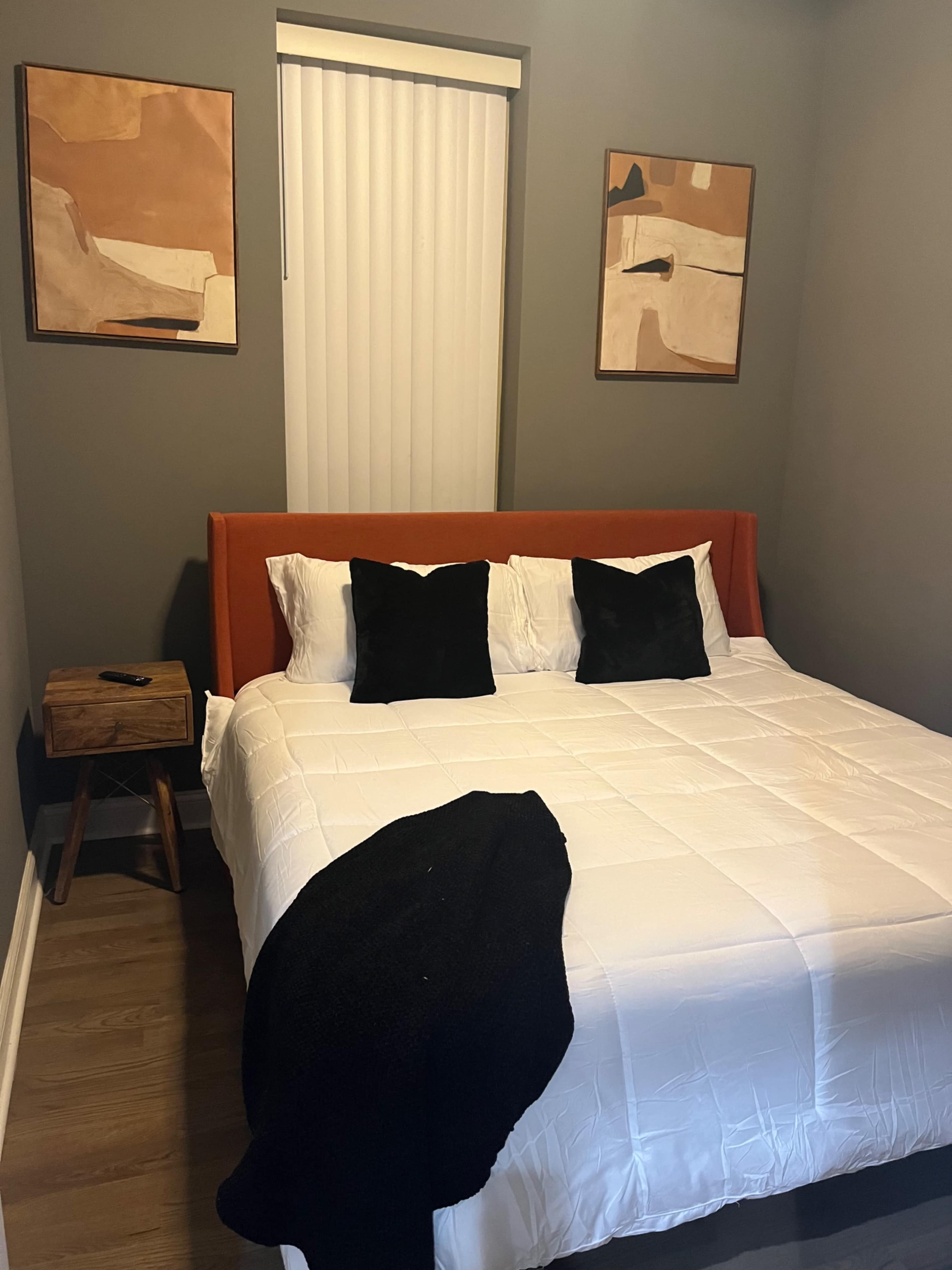 A simple bedroom with a bed, two decorative paintings on the wall, a wooden nightstand, and a black blanket draped over the bed.