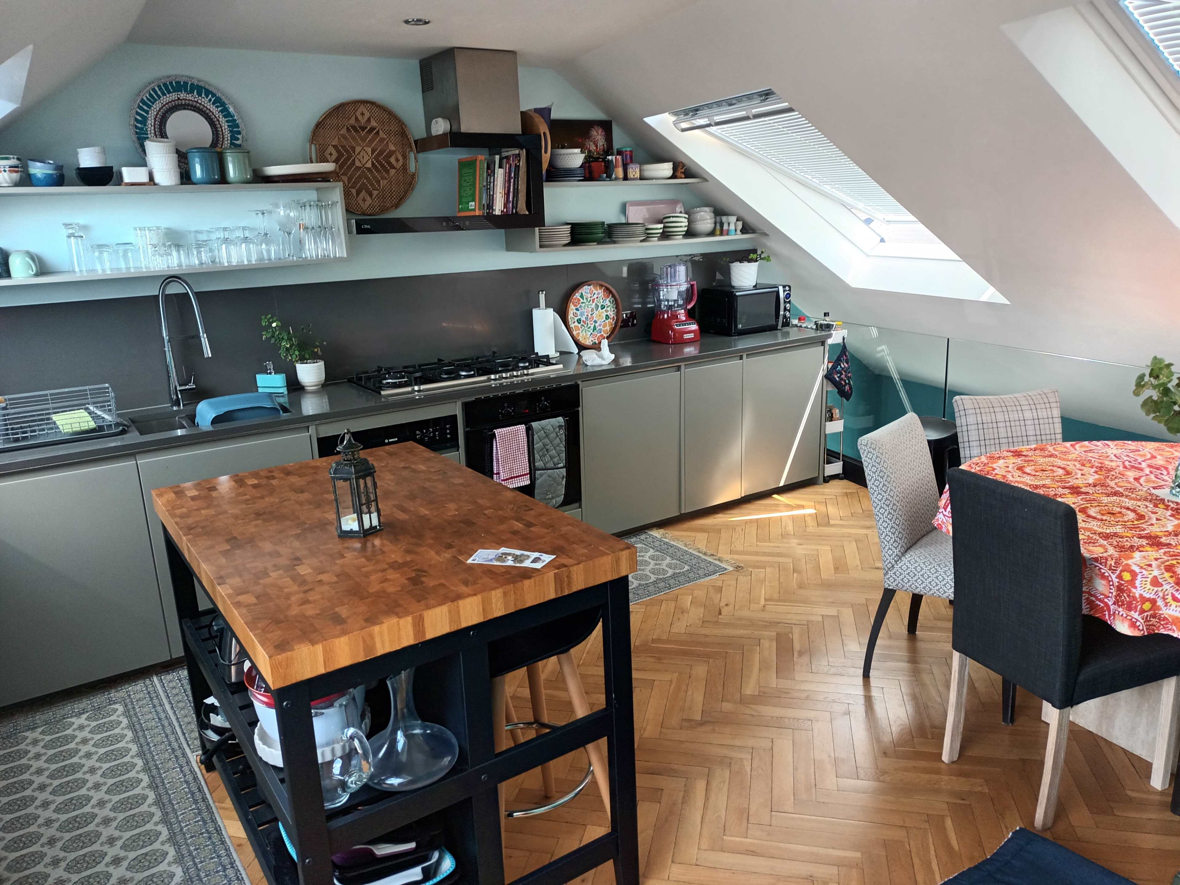 A modern kitchen with a wooden island, gray cabinets, and a dining area, all set in an attic space with sloped ceilings.
